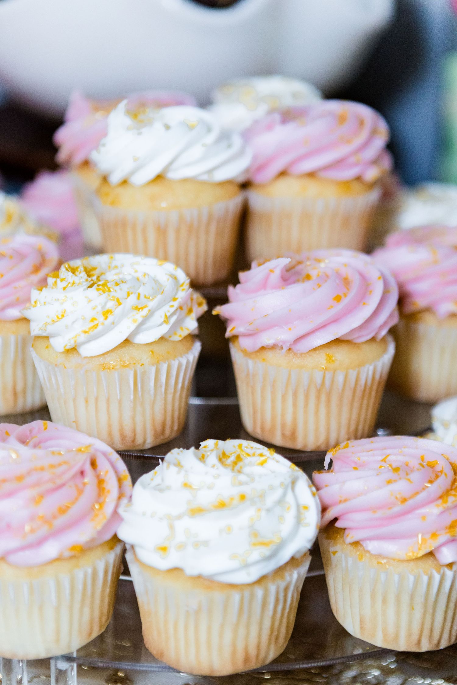 Elegant cupcakes with pink and white frosting topped with gold sprinkles arranged on a display.