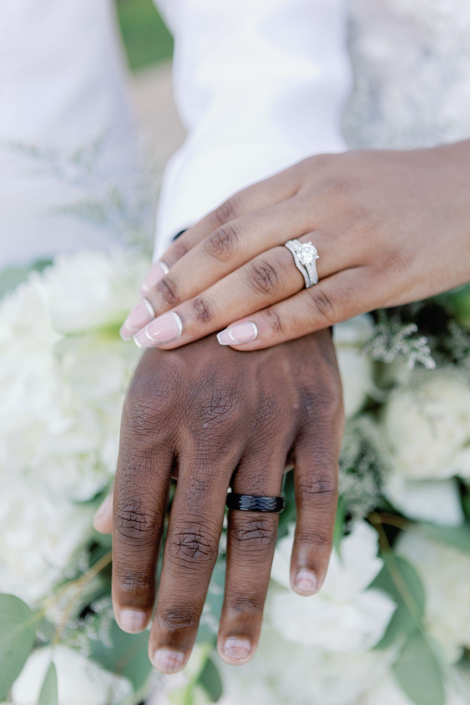 Close-up of wedding rings on hands with white floral decor in the background.