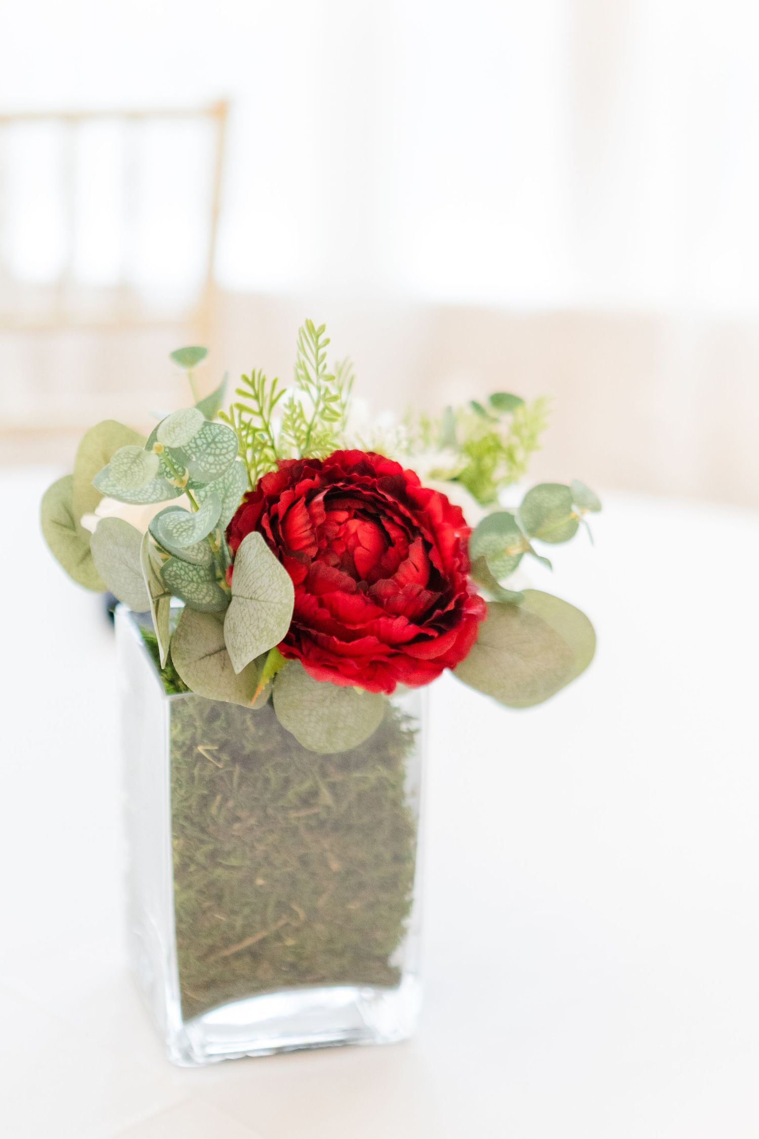 Red peony arrangement with eucalyptus in a modern square glass vase.