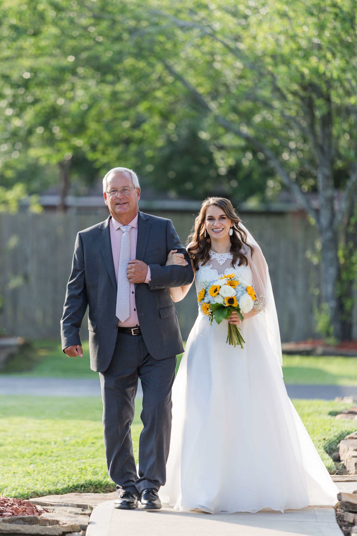 Outdoor wedding processional on green lawn with sunflower bouquet and formal attire.