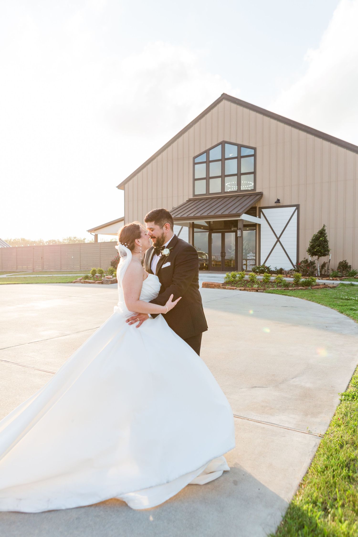 Elegant wedding couple dancing outside a modern farmhouse venue at golden hour.