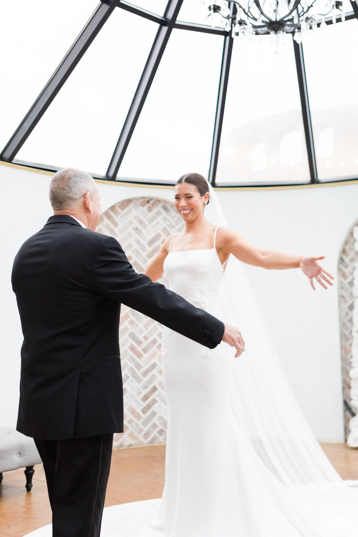 Emotional first look moment between bride and father in sunlit wedding venue.