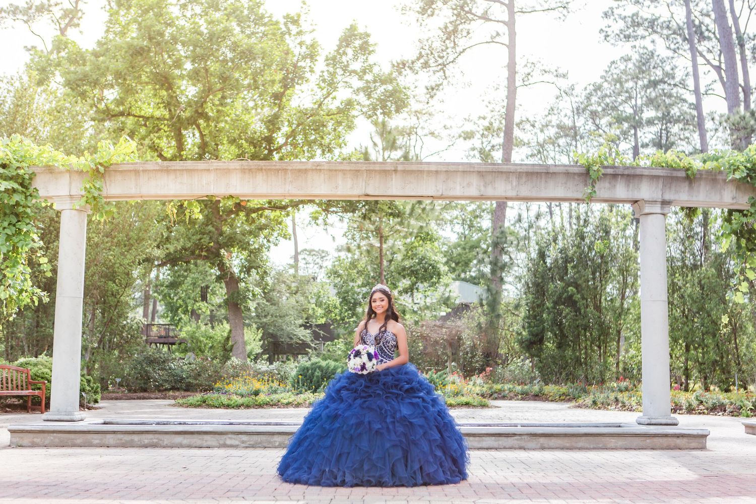 Elegant blue ballgown photographed in an outdoor garden setting with white columns.