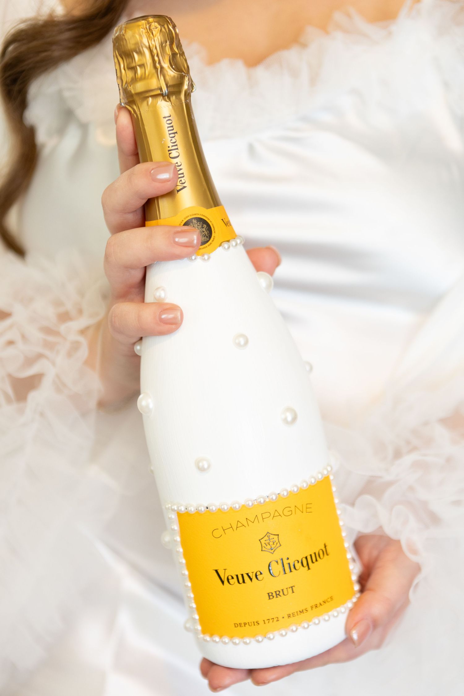 Veuve Clicquot champagne bottle in white and gold being held against white fabric.