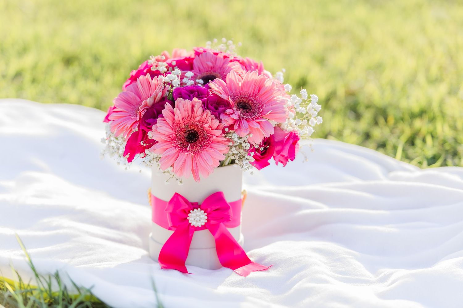 Bright pink gerbera daisies arranged on a white blanket in outdoor setting.