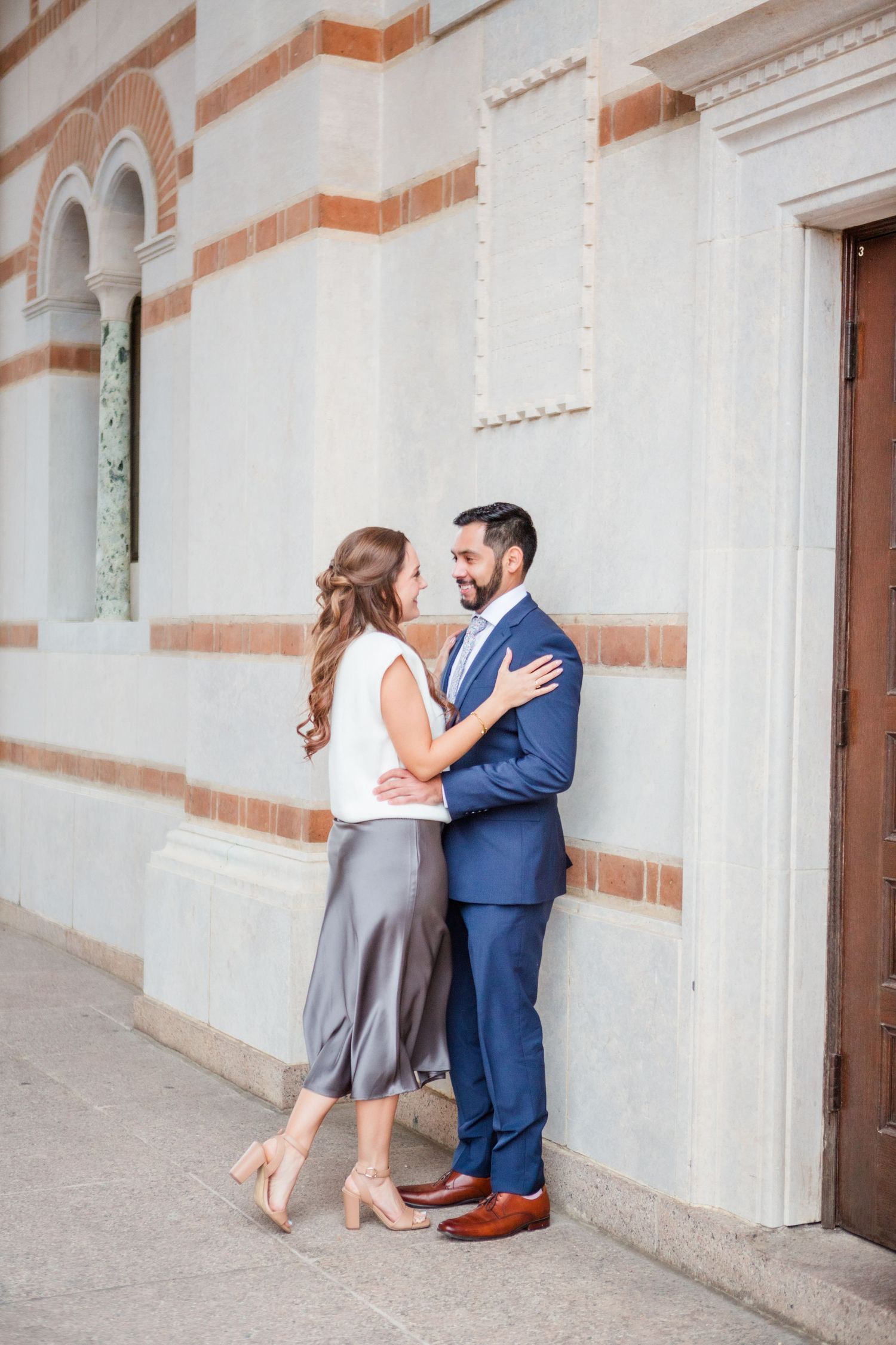 Romantic photoshoot along a historic building's exterior with arched doorways and brick accents.