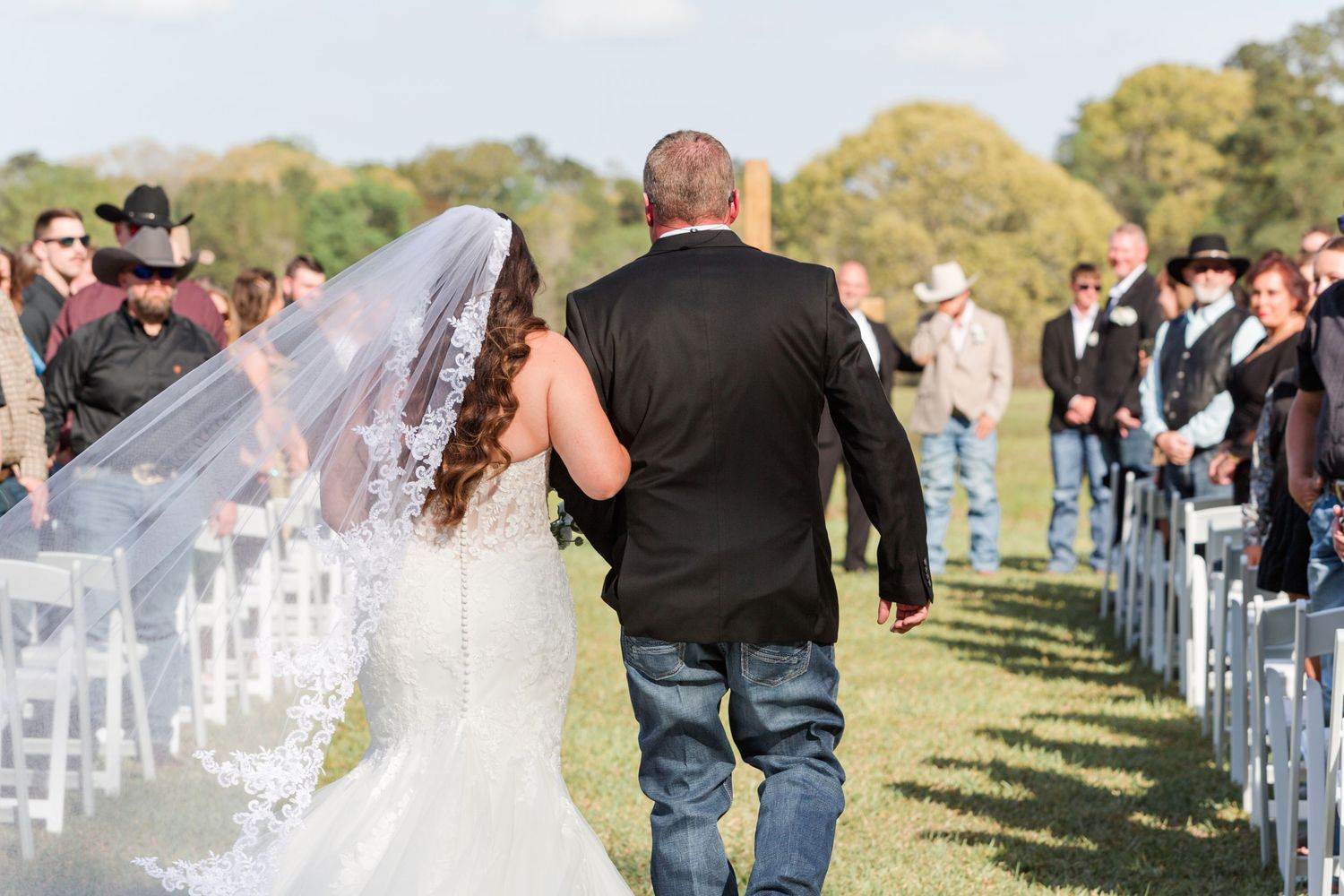 Outdoor wedding ceremony setup with white chairs and guests in attendance.