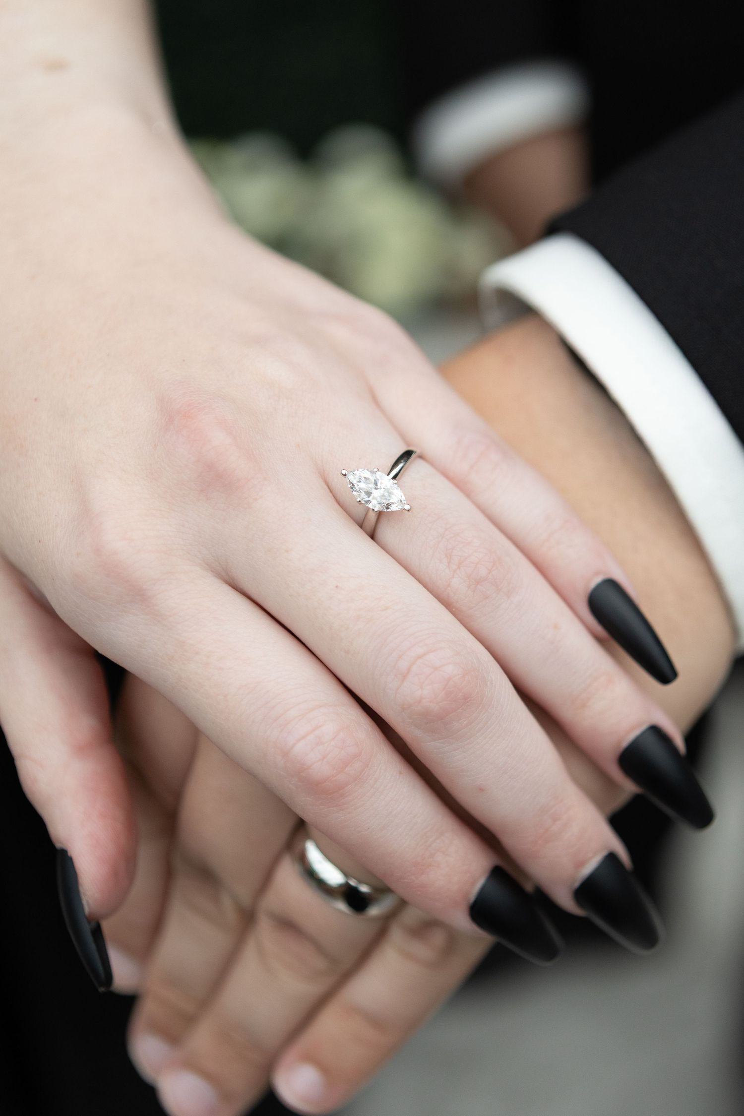 Close-up of engagement ring with black nail polish against wedding attire.