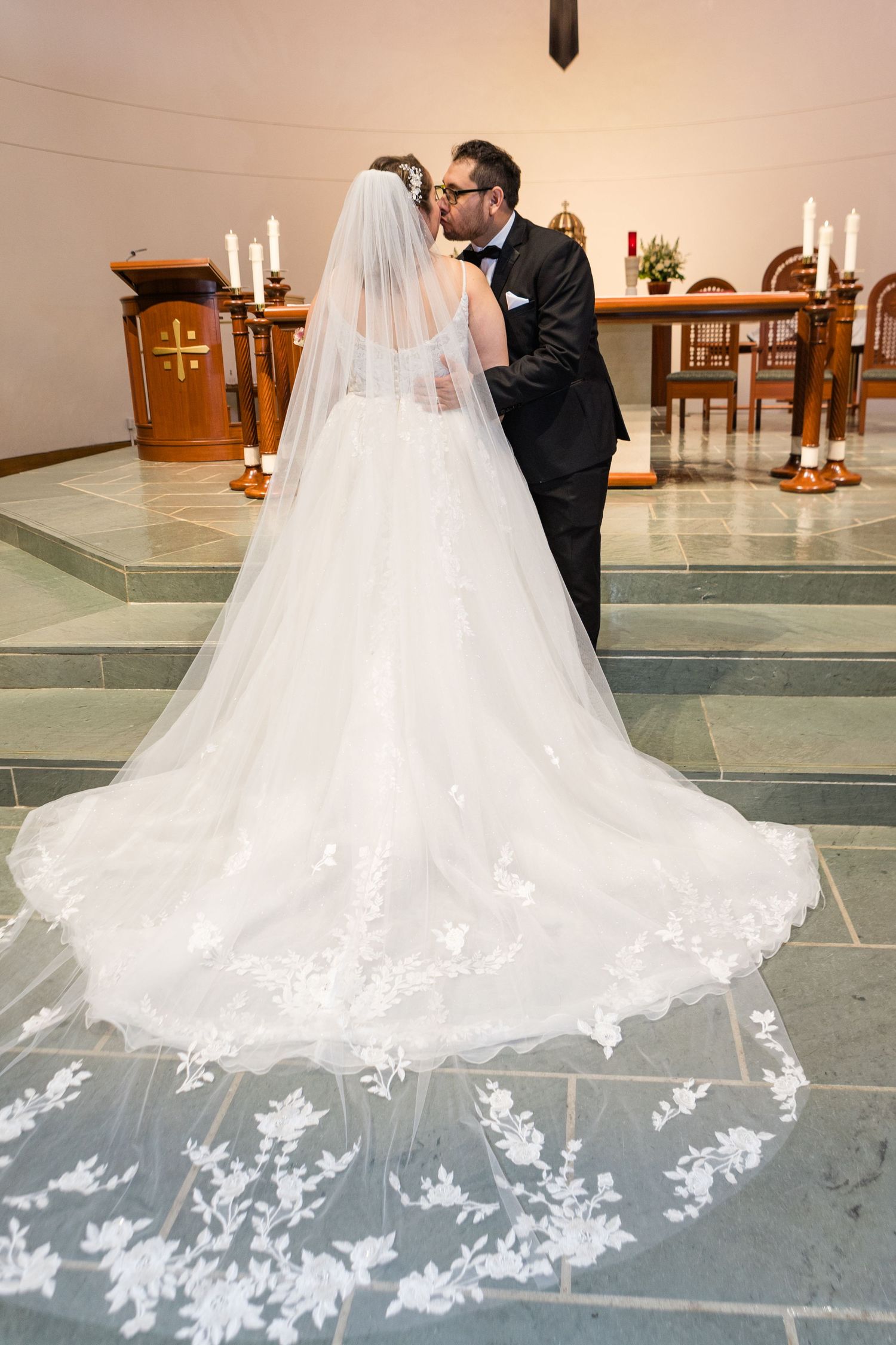 Detailed view of an ornate lace wedding dress train spread across church floor tiles.