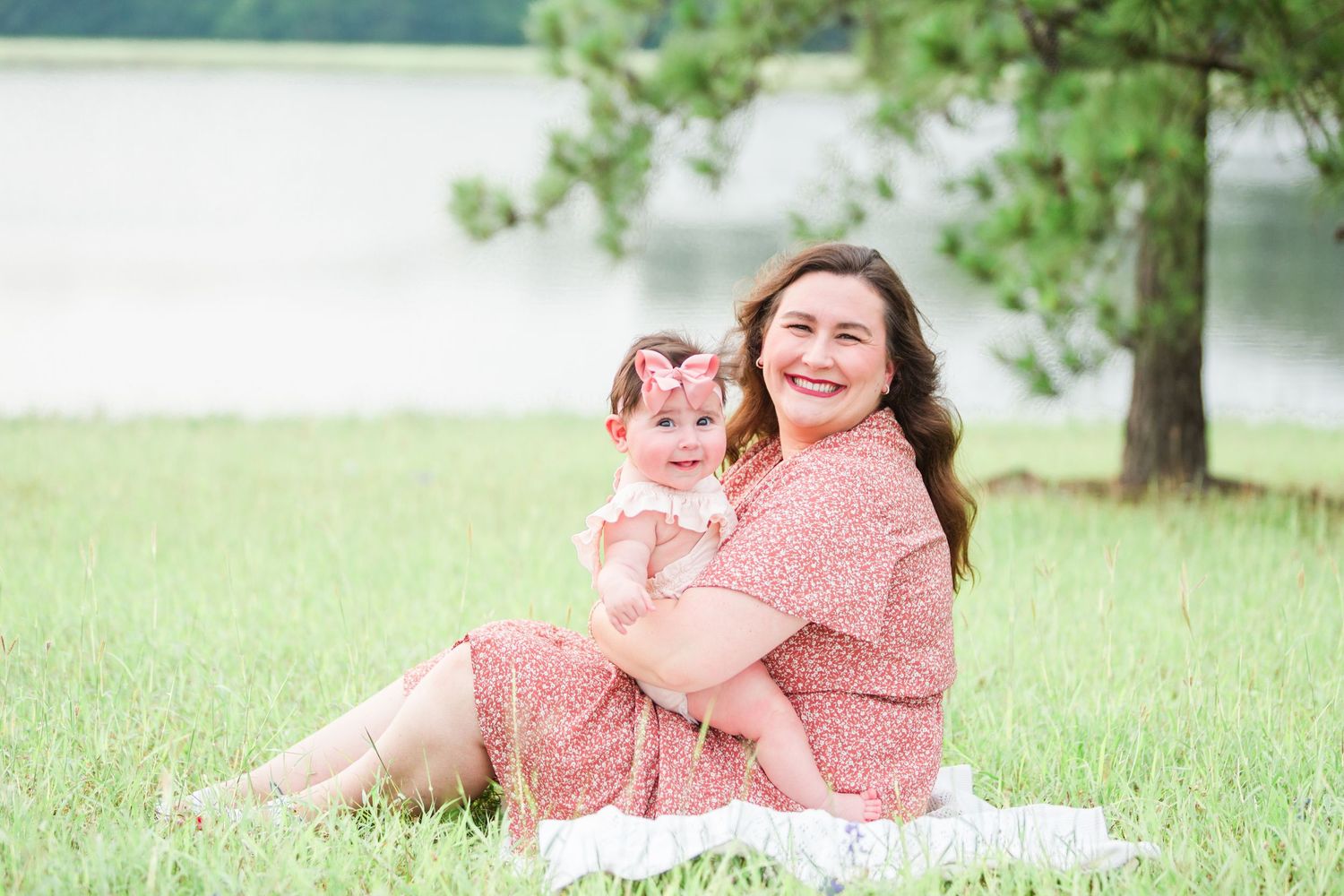 Mother and daughter in matching coral outfits sitting together on grass near a lake.