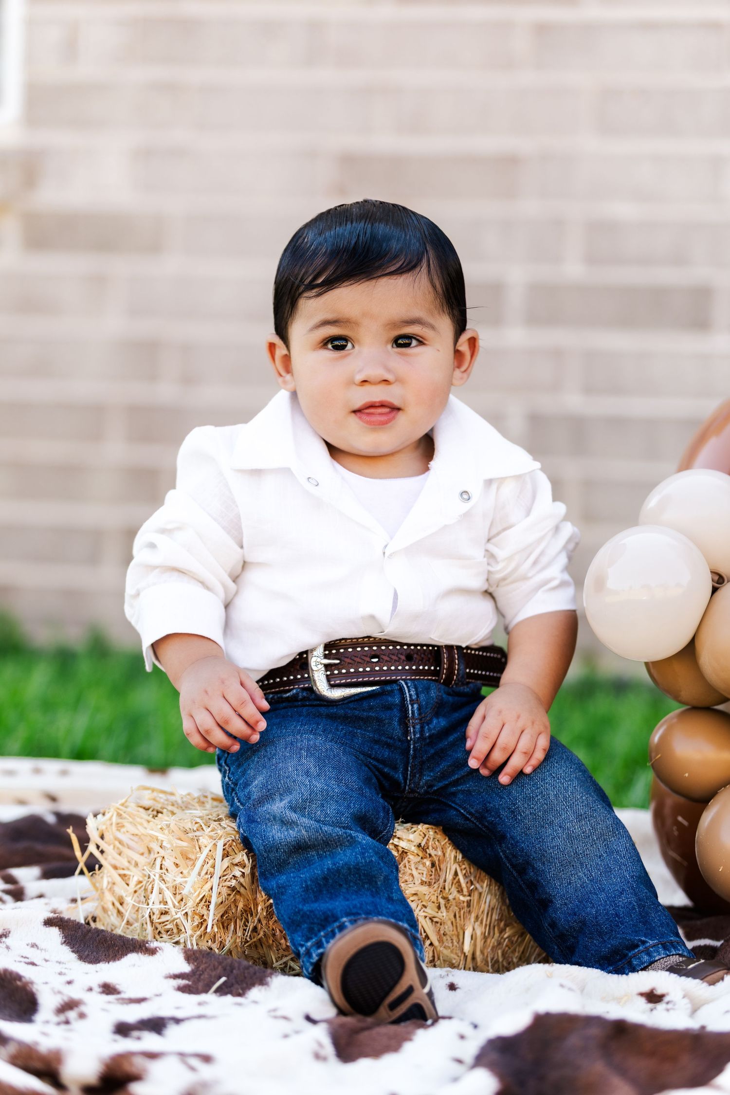 Young child in white shirt and jeans sits on hay bale with party decorations.