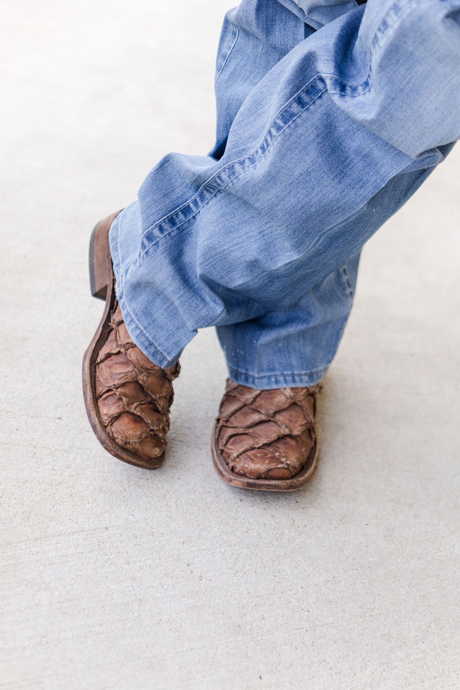 Close-up of brown leather cowboy boots with blue jeans on a light colored floor.