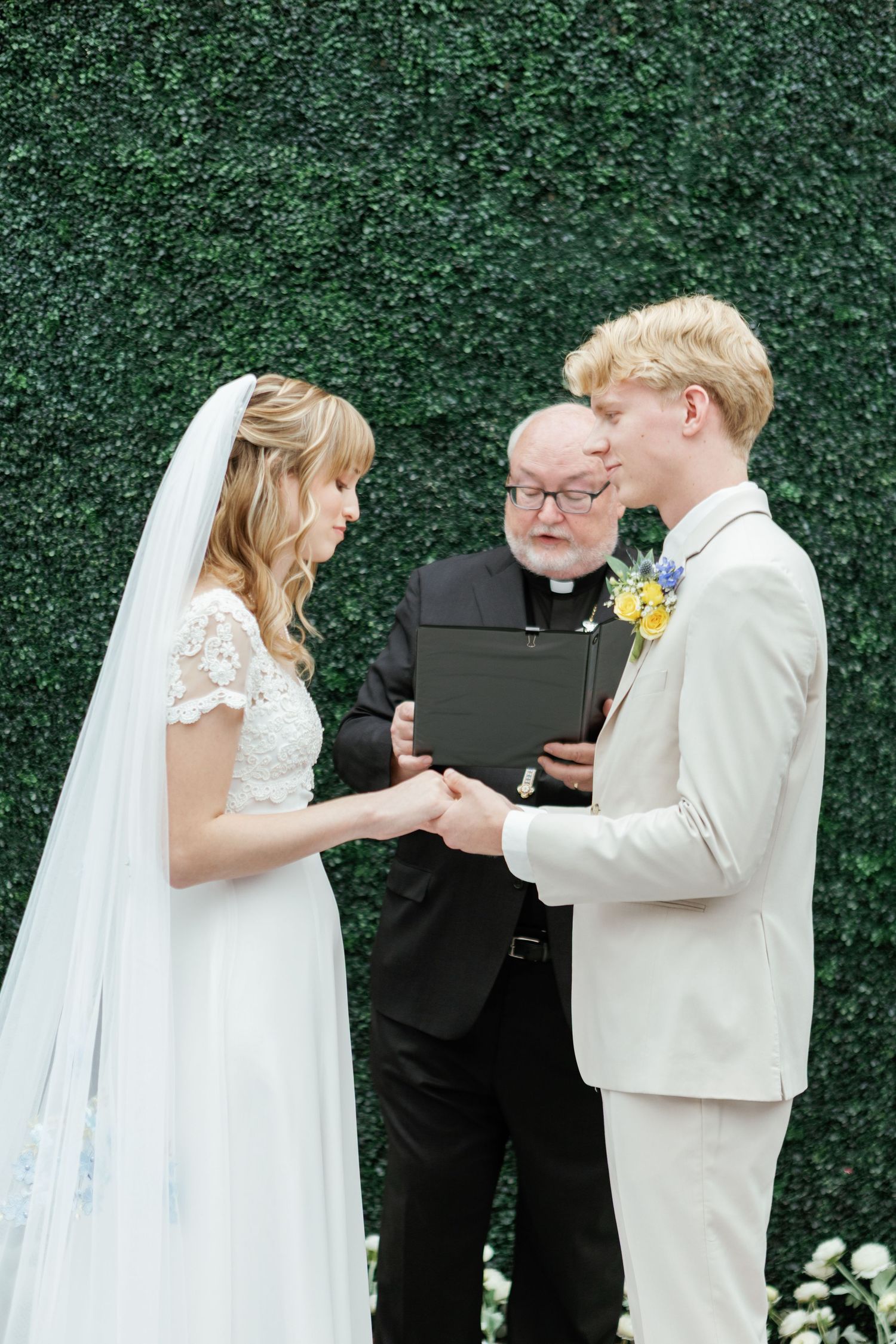 Wedding ceremony with couple and officiant exchanging rings against greenery backdrop.