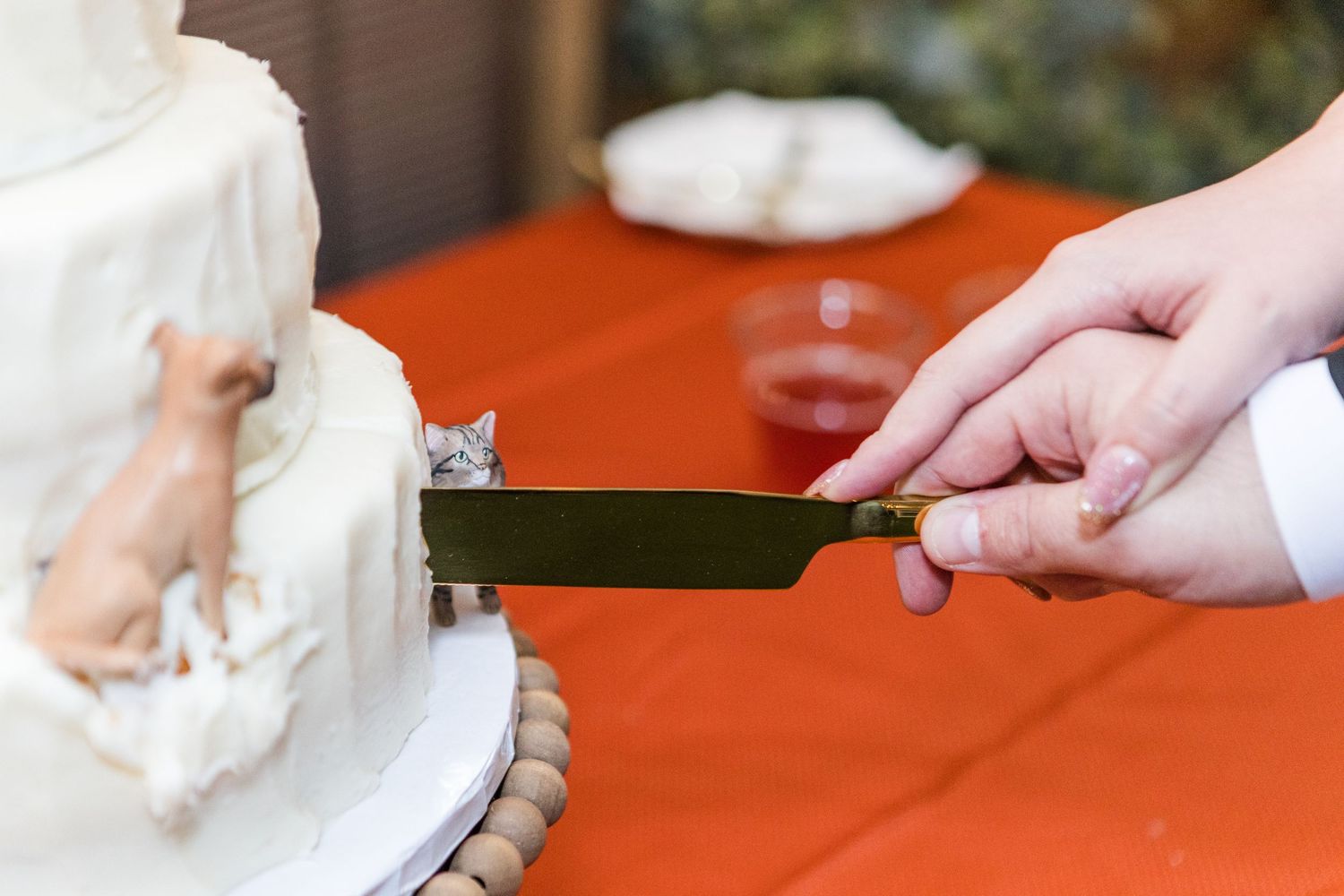 Chef hands in white gloves slicing raw chicken breast on an orange cutting board with a sharp knife.