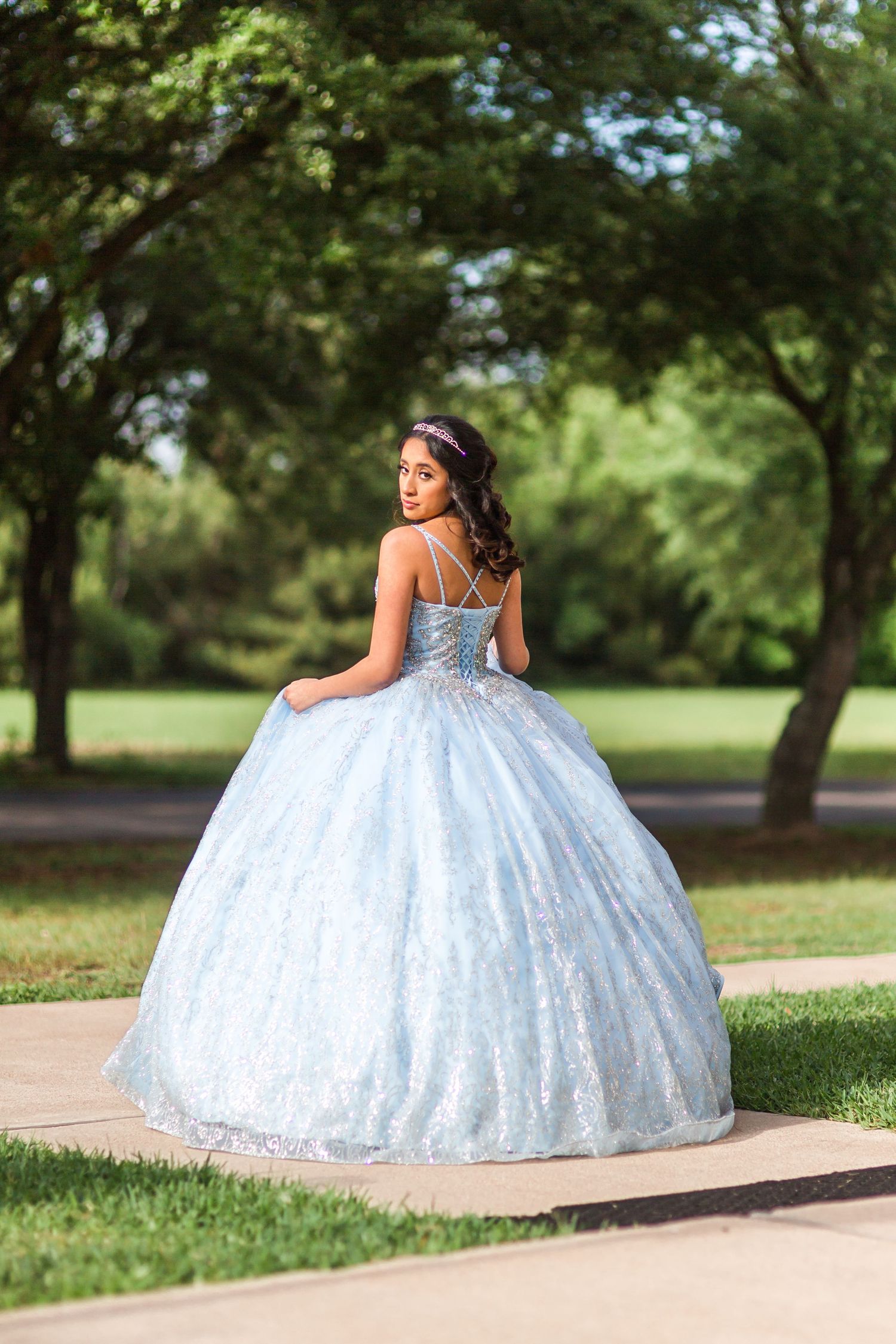 Flowing light blue princess ball gown photographed in a sunny park setting.