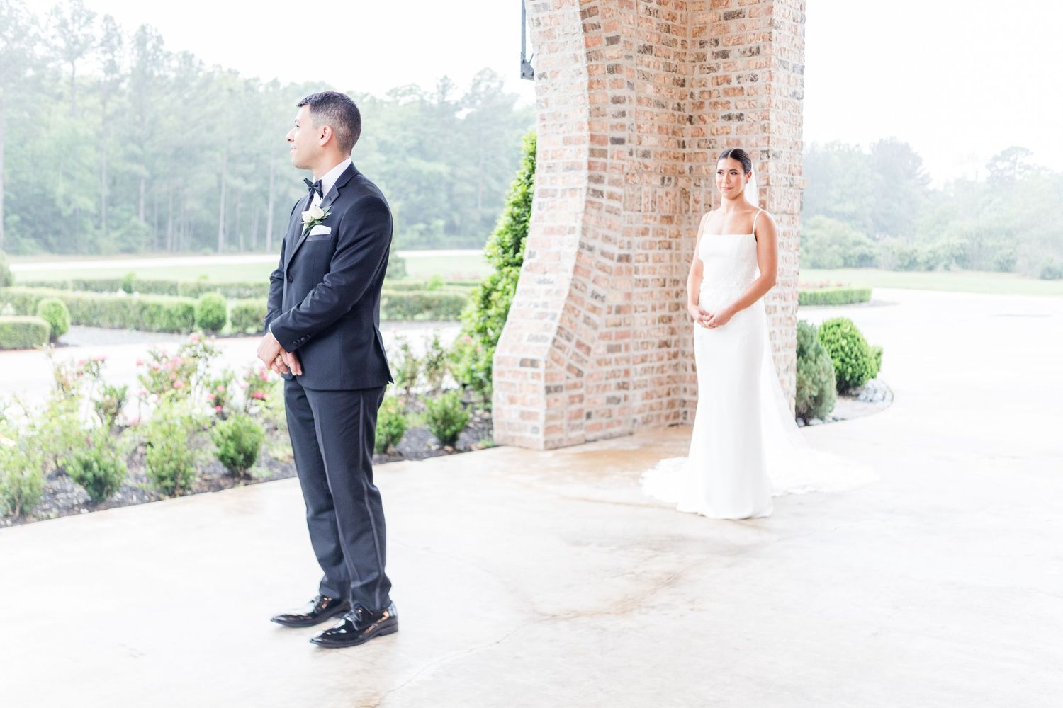 A couple shares a first look moment on a brick-pillared terrace.