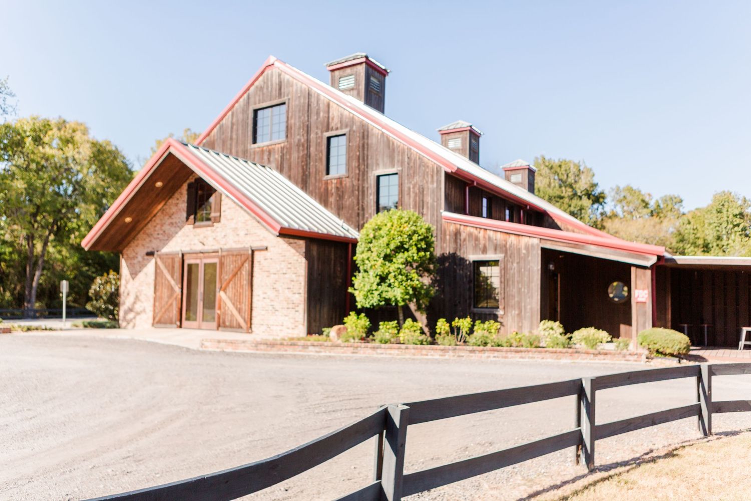 Modern farmhouse wedding venue with stone accents and wooden barn doors behind black fence railing.