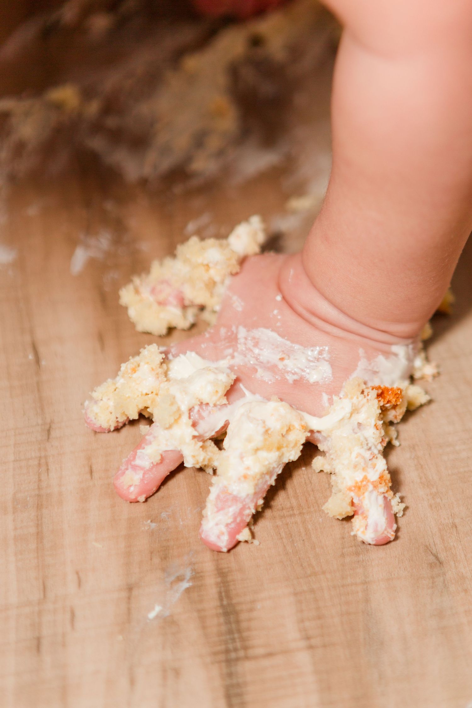 Close-up of a small hand covered in cake and frosting on a wooden surface.
