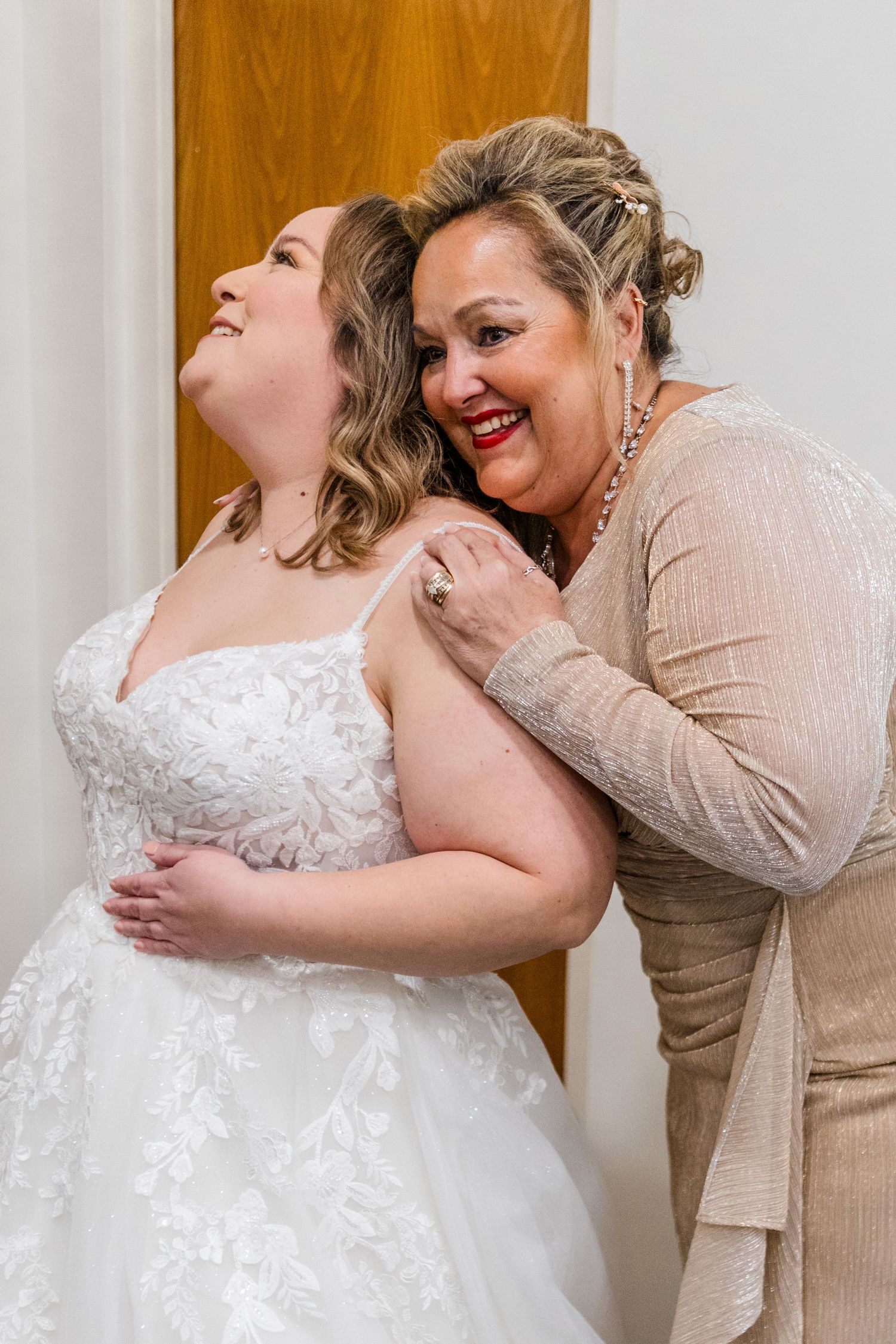 Joyful moment between bride in white dress and woman in beige outfit.