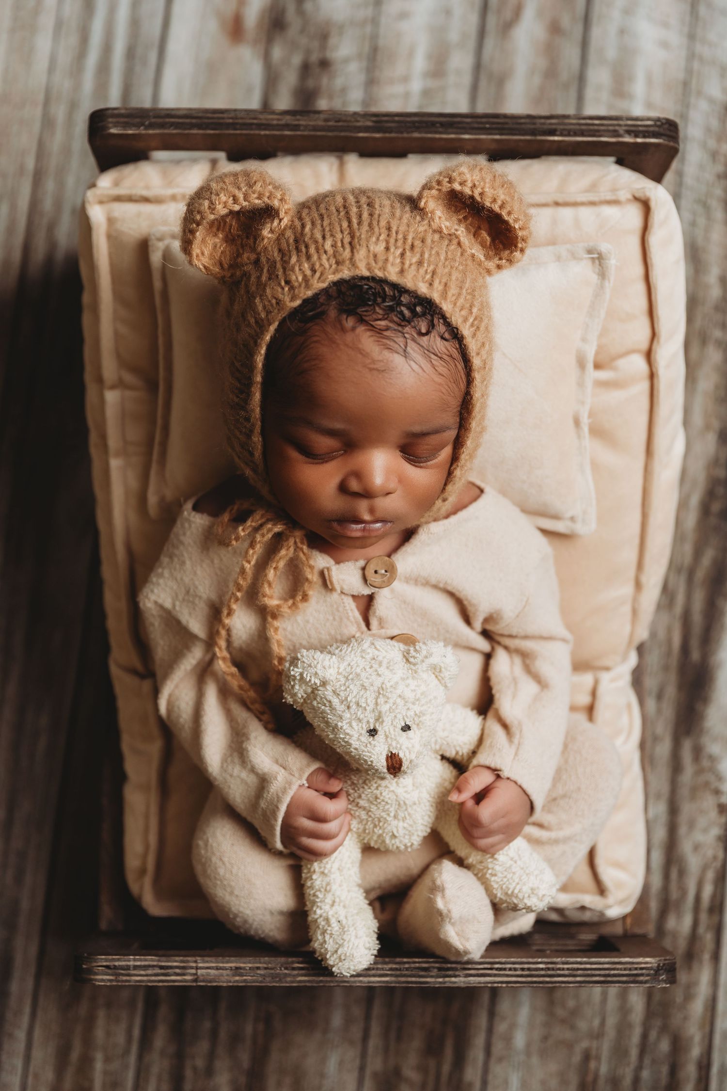 Newborn baby boy lays on prop bed holding teddy bear and wearing hat with ears during photoshoot with Tami Harris Photography in Worthington