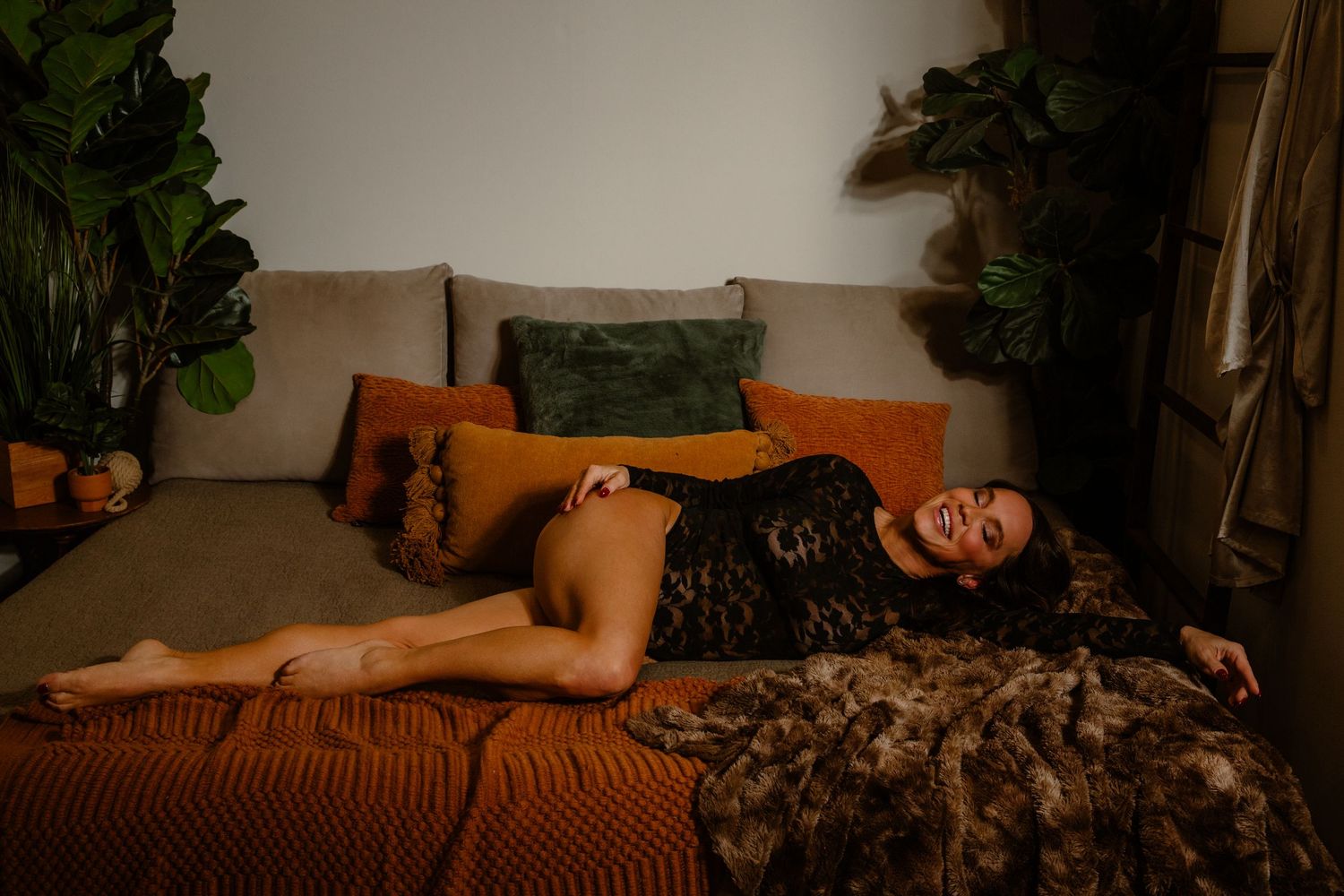 woman in black lace bodysuit smiles while lying in bed full of pillows for boudoir portrait photoshoot in central ohio Worthington