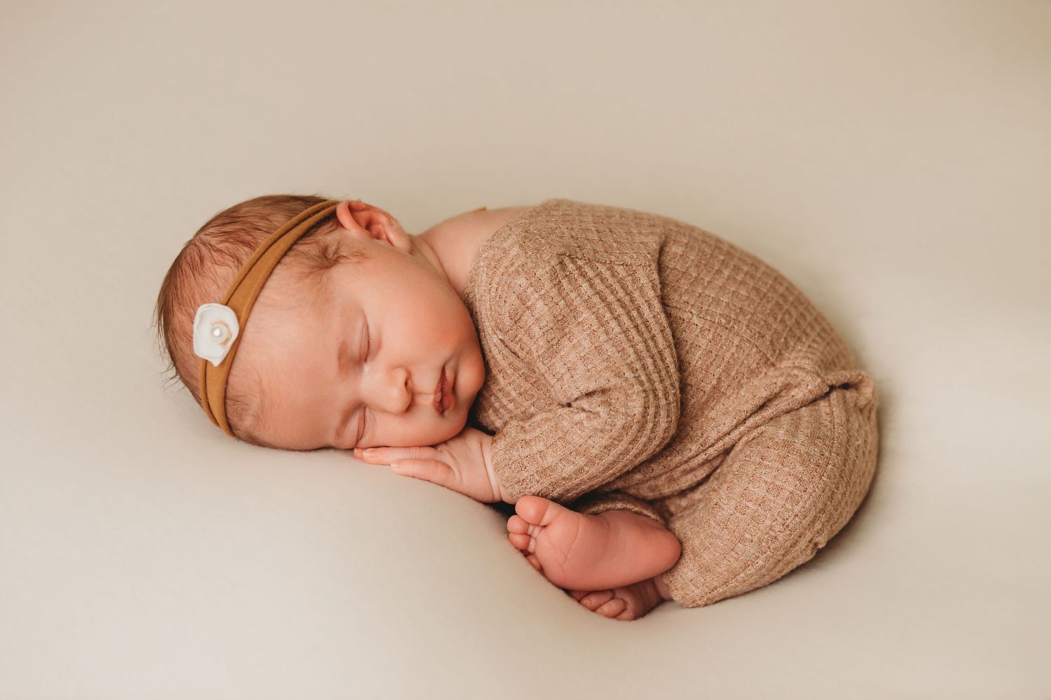 Baby girl in neutral newborn romper lays sleeping with feet exposed during photo session with Tami Harris Photography in Columbus Ohio