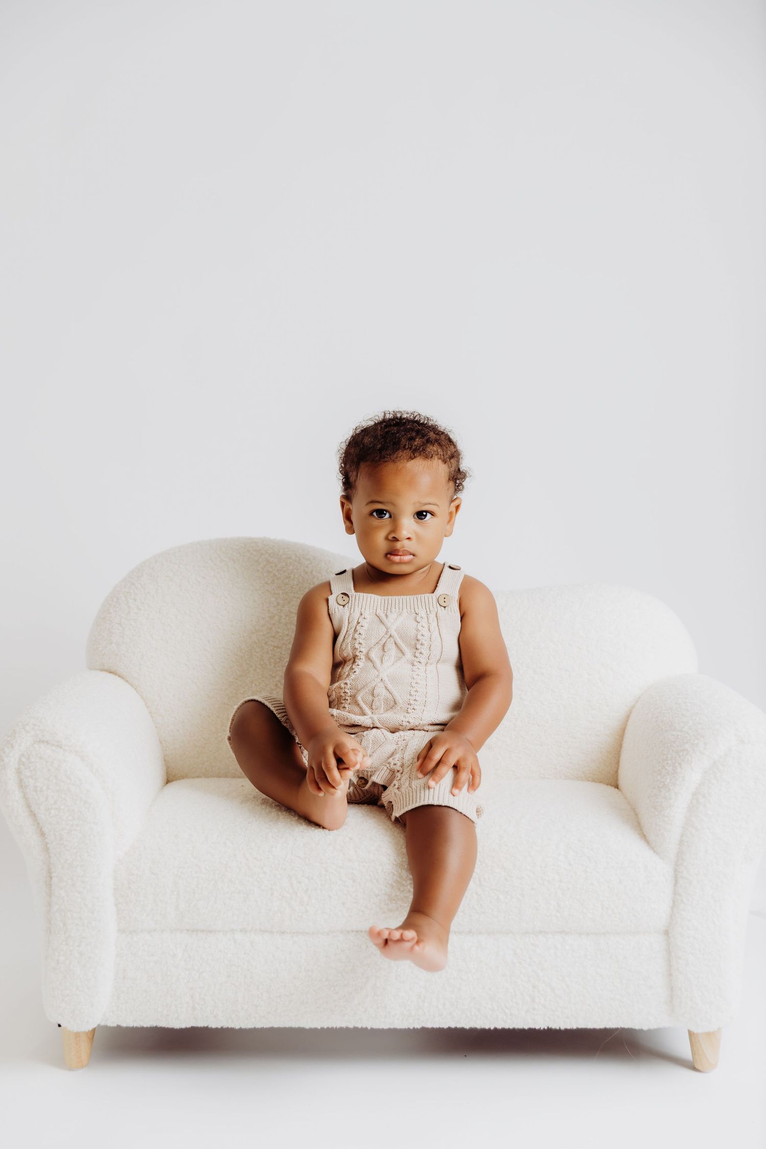 Baby boy sitting on child-size couch holding his foot during 1st birthday photoshoot with Tami Harris Photography in Columbus Oh area studio