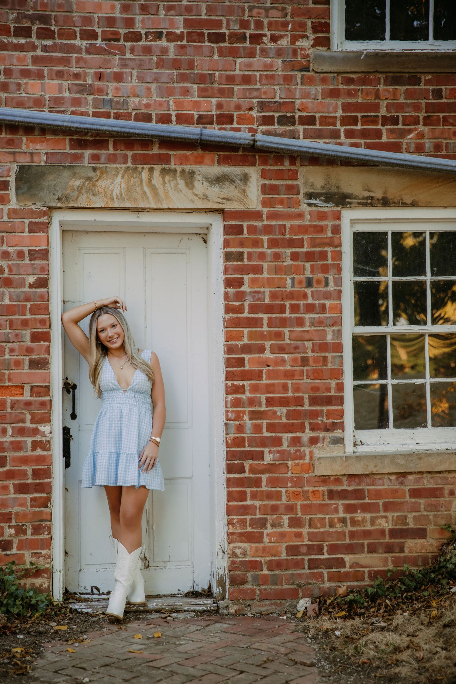 Graduating senior girl in dress and cowboy boots leans on door frame at Homestead Park in Westerville for photoshoot session
