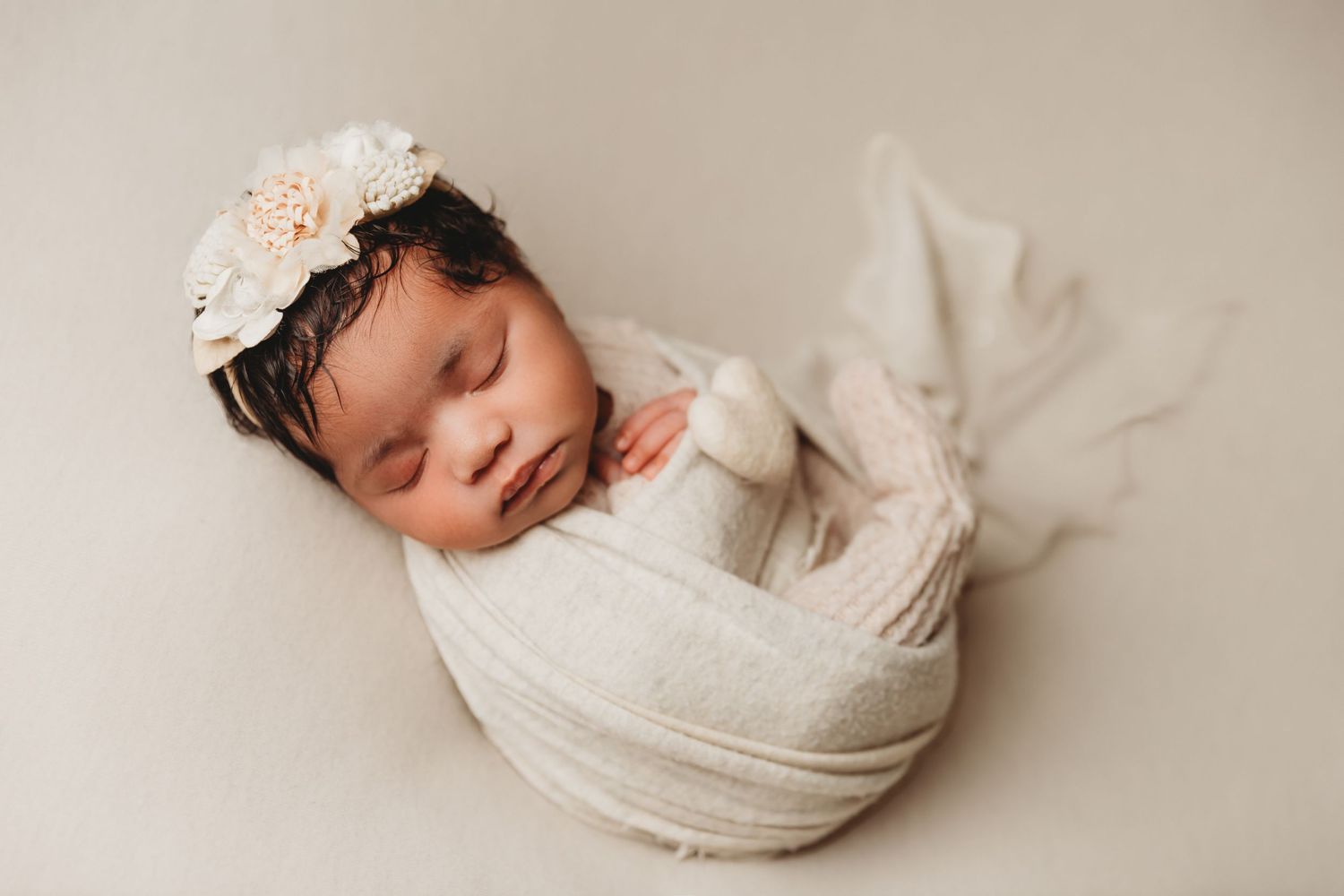 Baby girl sleeps wrapped in creamy white swaddle and matching floral headband for newborn photos with Tami Harris Photography in Central Oh