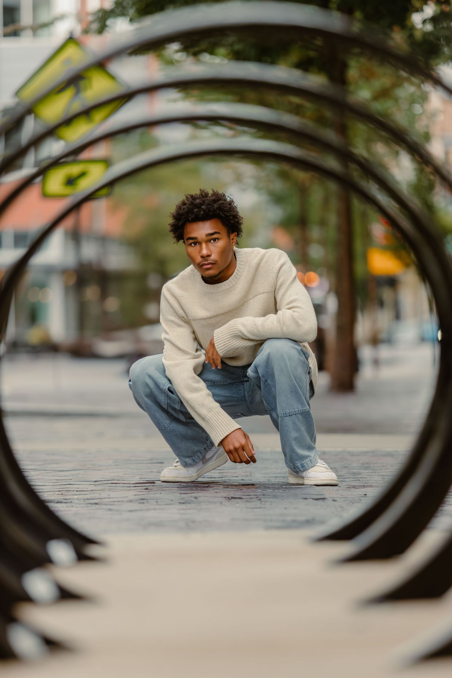 High school senior portrait of boy in jeans and a sweater, shot dramatically through bike rack in Bridgepark in Dublin, Ohio.
