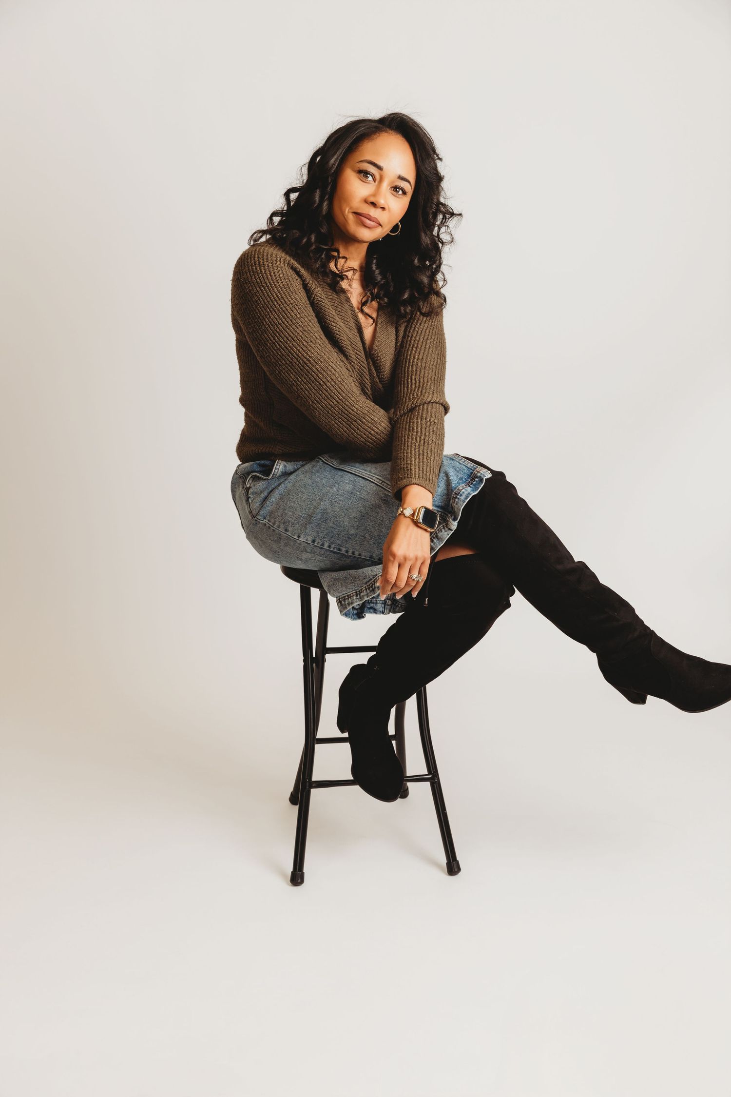 Branding Photo of black female photographer wearing sweater and jean skirt sits on black stool in a Columbus Ohio photography studio setting