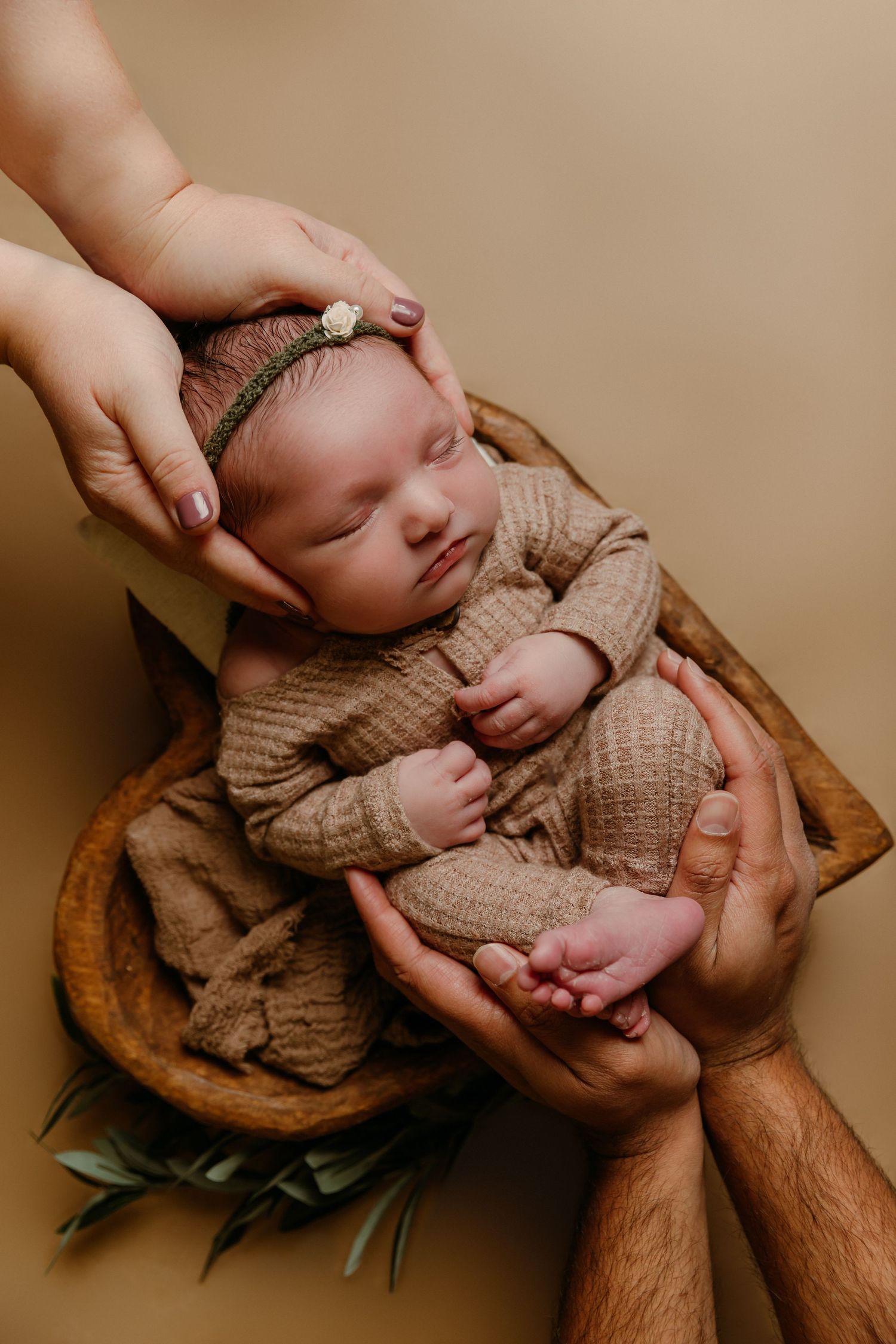 Newborn baby girl rests sleeping in parents' hands in heart-shaped wooden bowl for photoshoot with Tami Harris Photography in Worthington Oh
