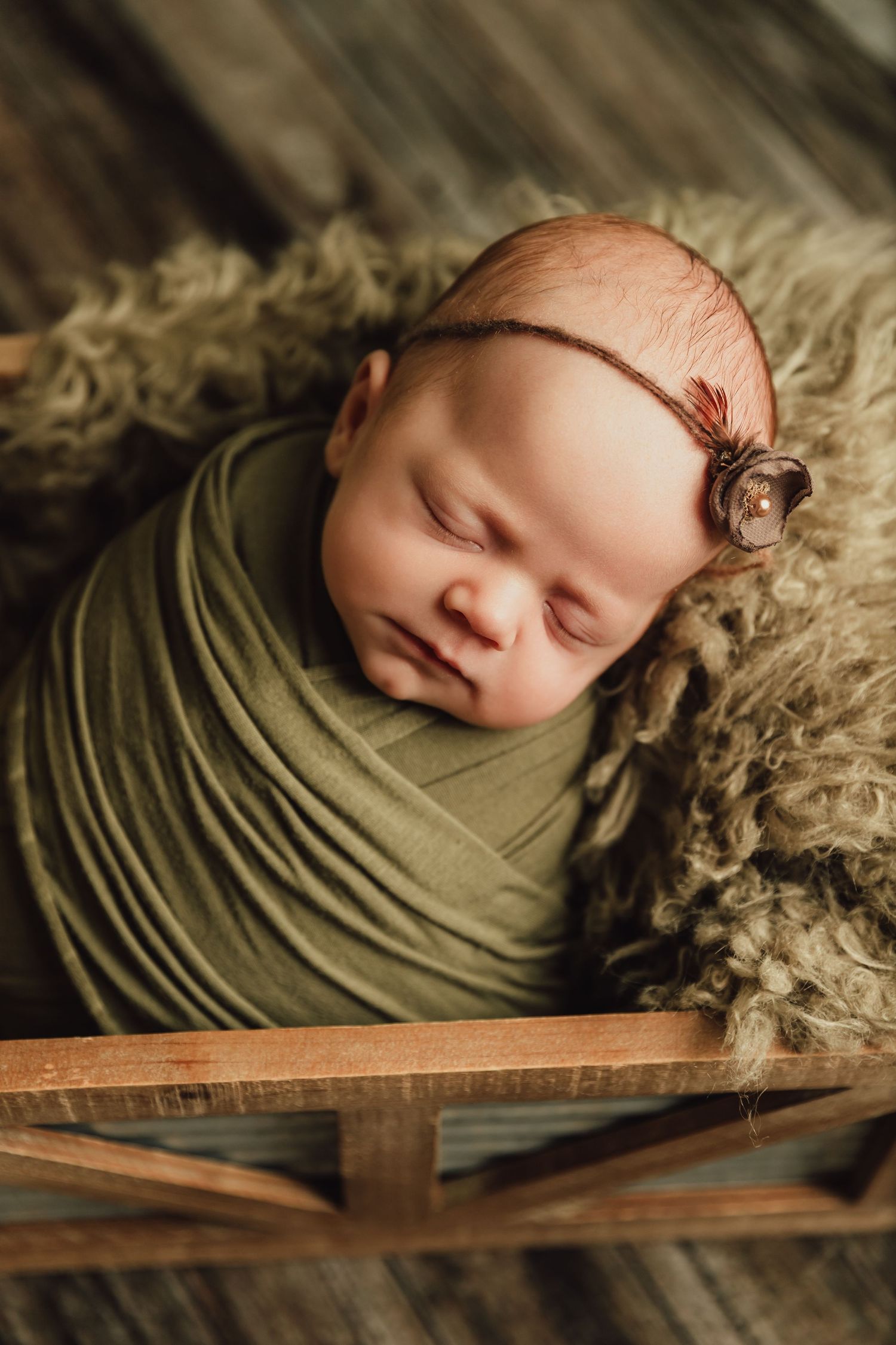 Newborn baby girl leans on green fur layer while lying in a wooden crate during newborn portrait session with Tami Harris Photography