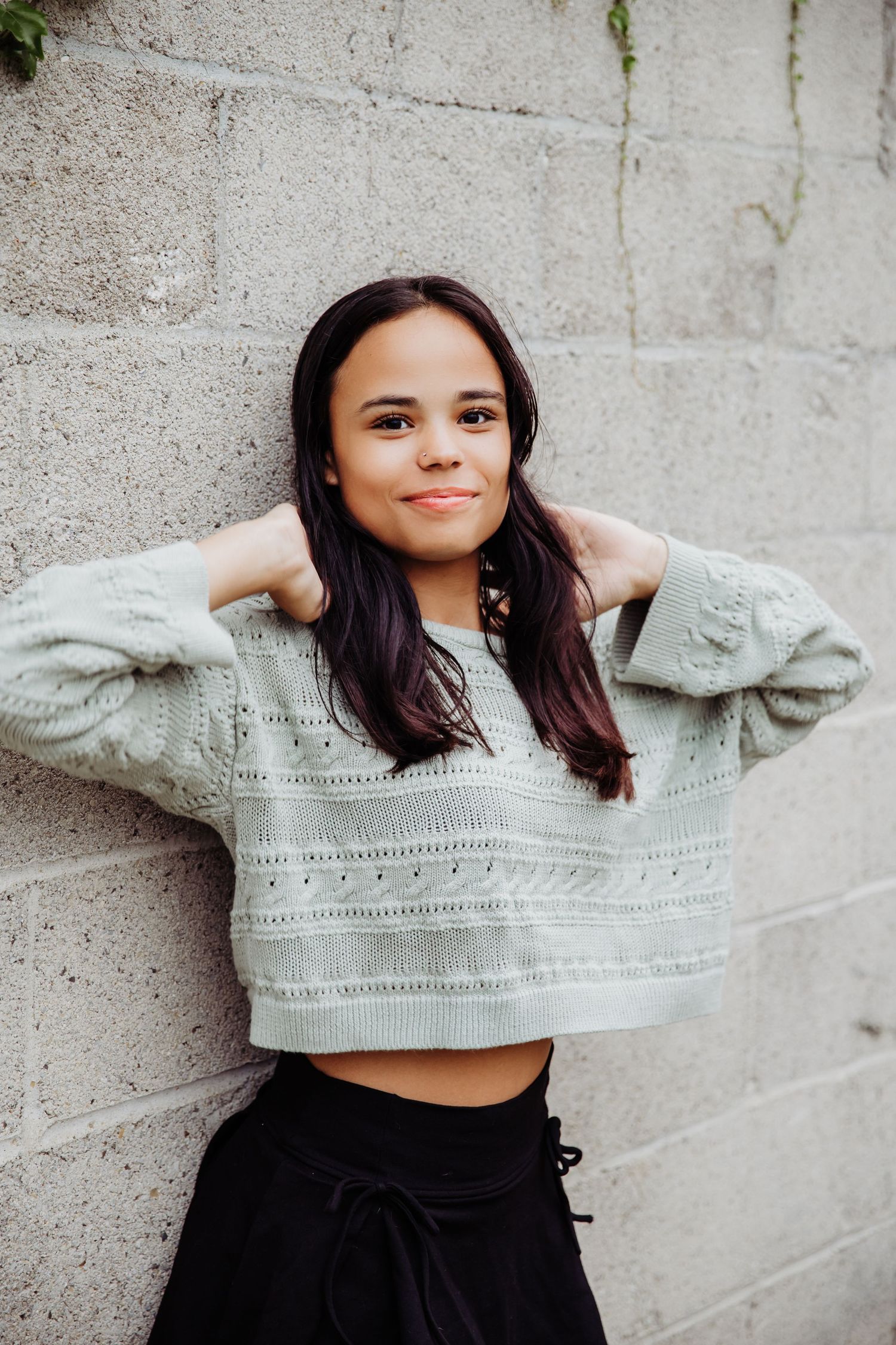 Senior girl smiles softly while playing with hair in front of brick wall in W, Ohio during portraits with Tami Harris Photography