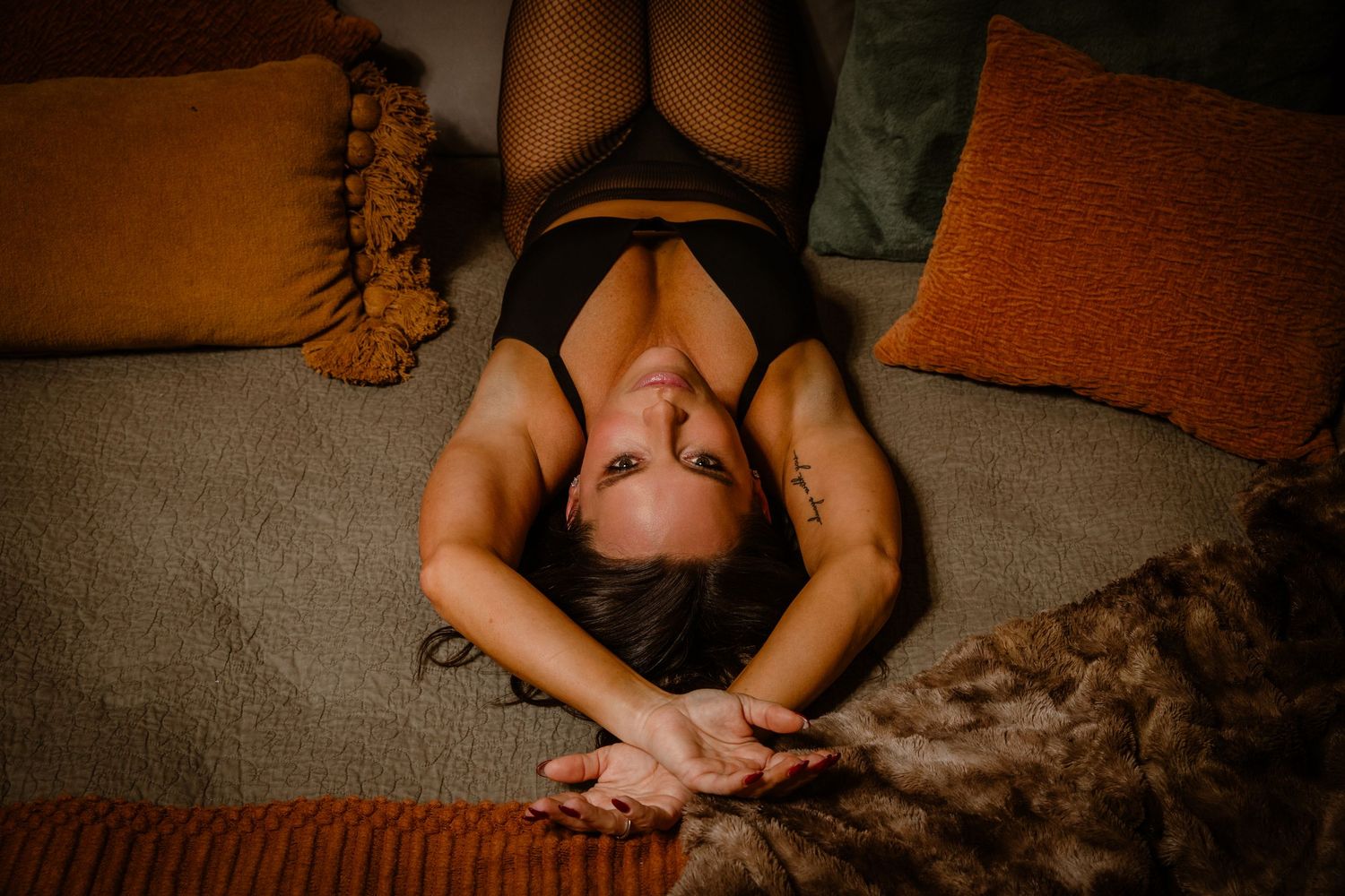 Overhead portrait of woman in black lingerie with arms above her head lying in bed for studio boudoir portrait session in Worthington, Ohio