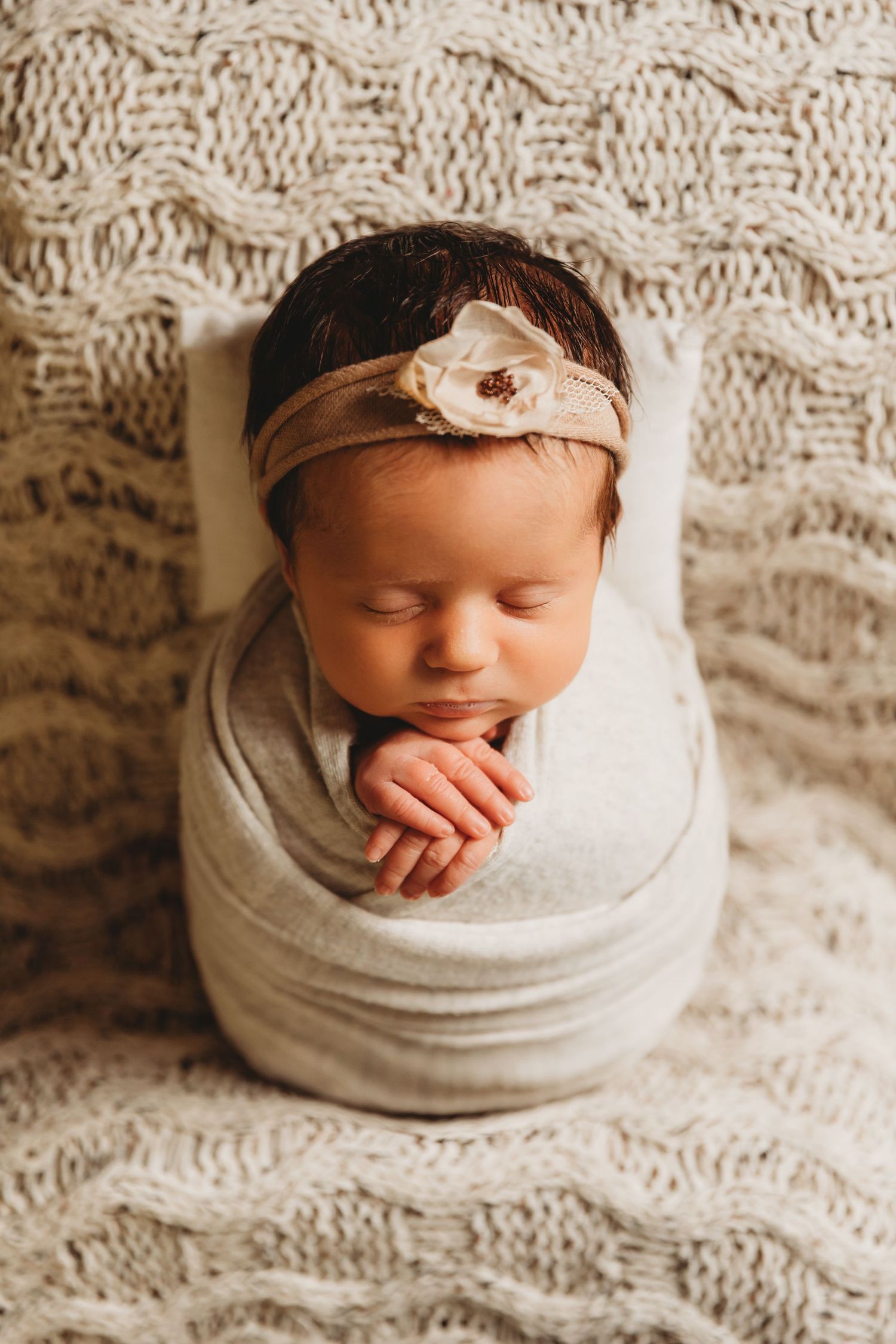 Newborn baby girl wrapped in cream swaddle and wearing a floral headband during photo session with Tami Harris Photography