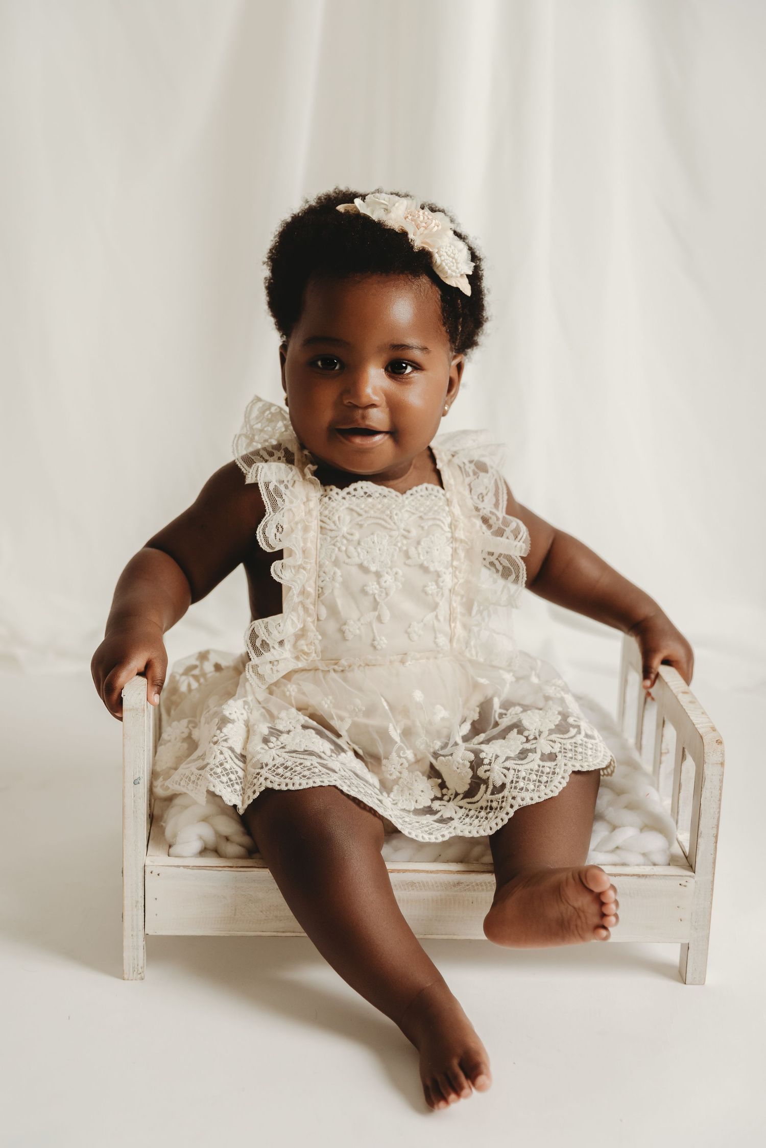 Smiling 1-year-old girl sits on white prop bed during Baby/Child Milestone session with Tami Harris Photography for 1st birthday