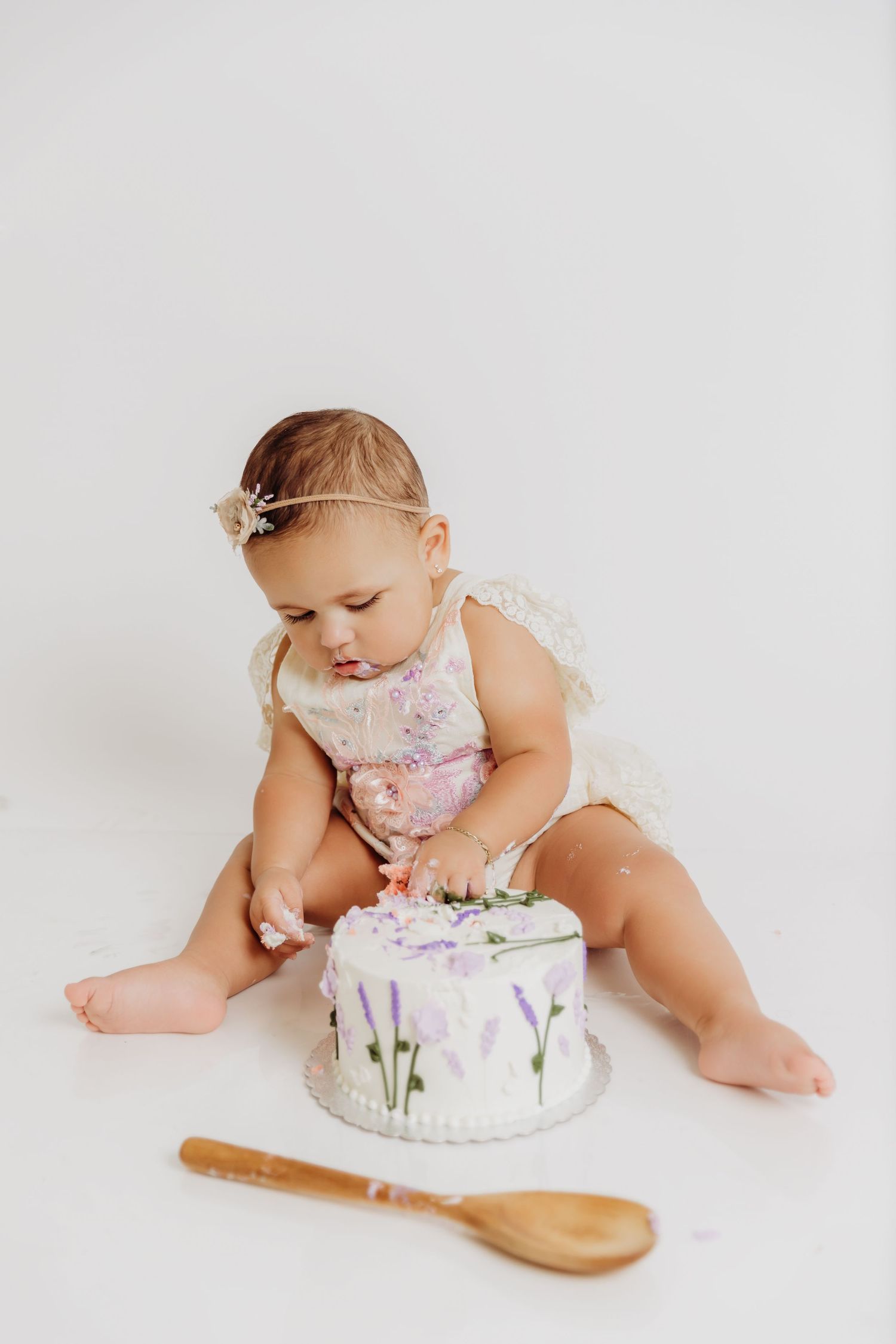 Baby girl sitting in front of birthday cake digging in with her hands for first birthday photos with Tami Harris Photography