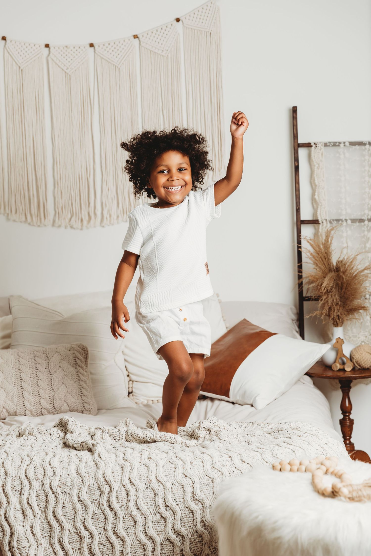 4-year-old boy with long curly hair jumps on bed during Milestone Birthday photoshoot with Tami Harris Photography