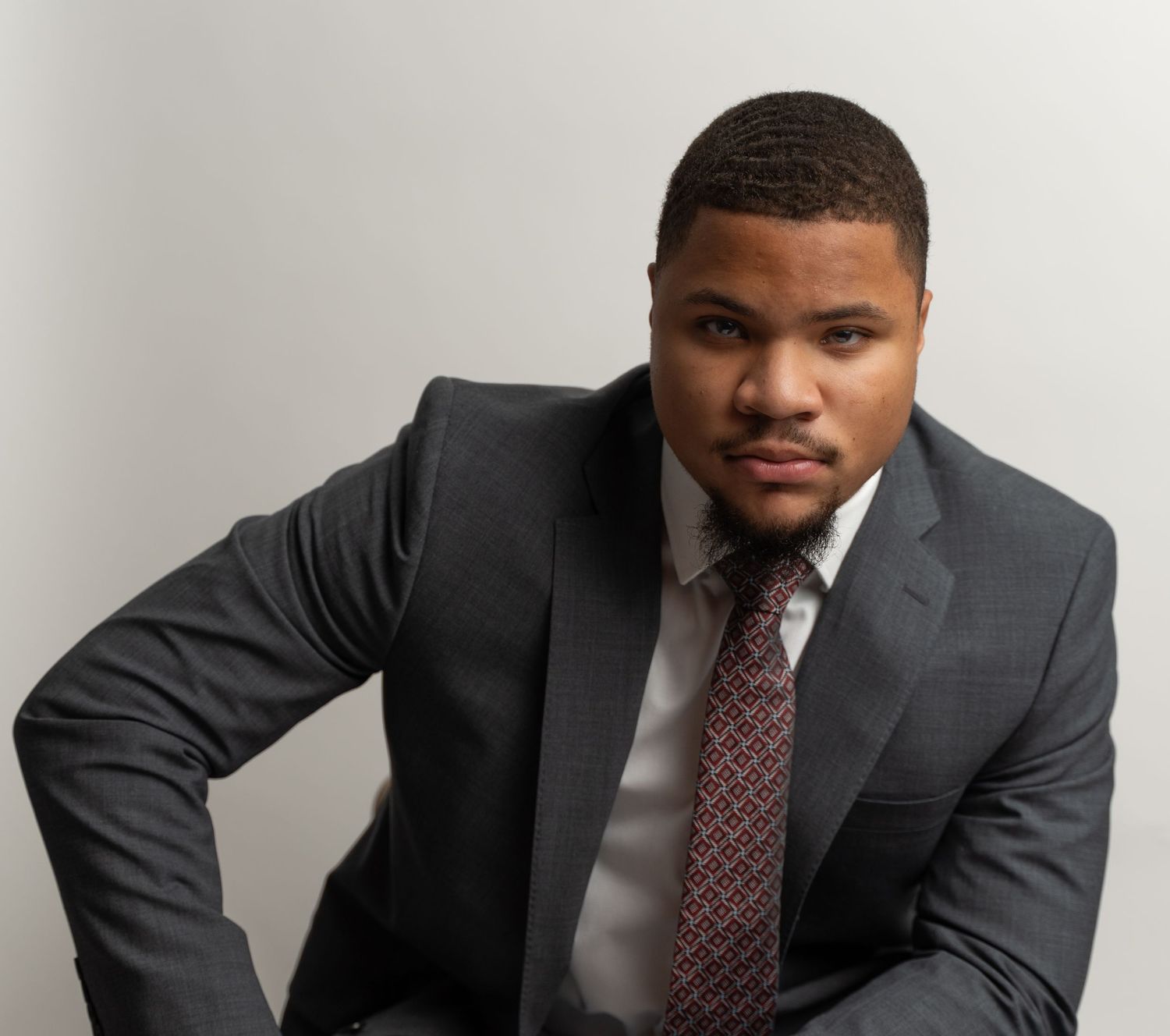 Professional headshot of someone in a dark suit and patterned tie against a light background.