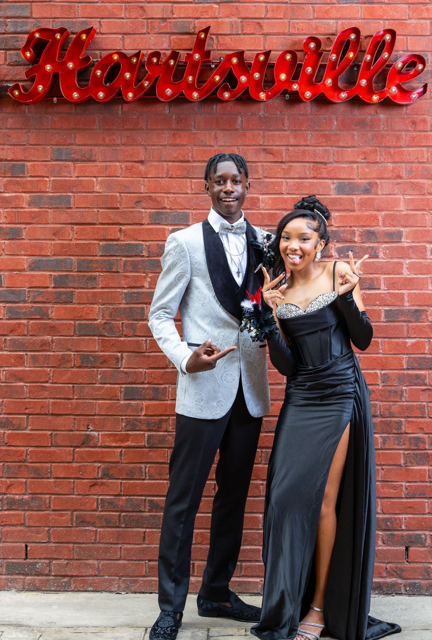 Formal couple posing in evening wear beneath red neon 'Nashville' sign on brick wall.