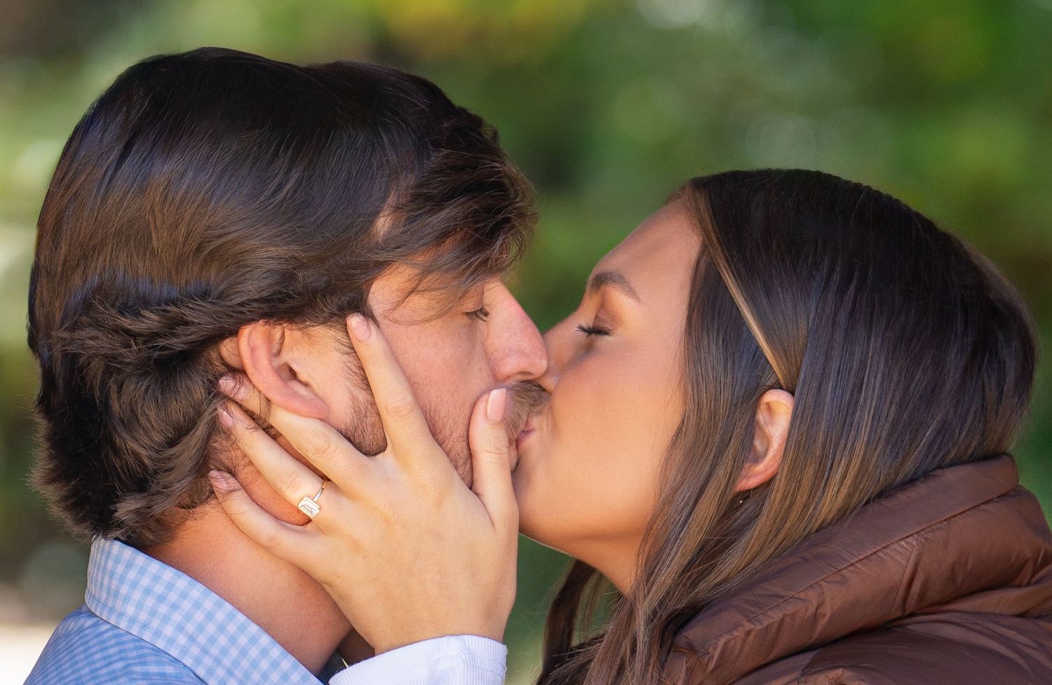 Romantic close-up of couple sharing intimate kiss outdoors while showing engagement ring.