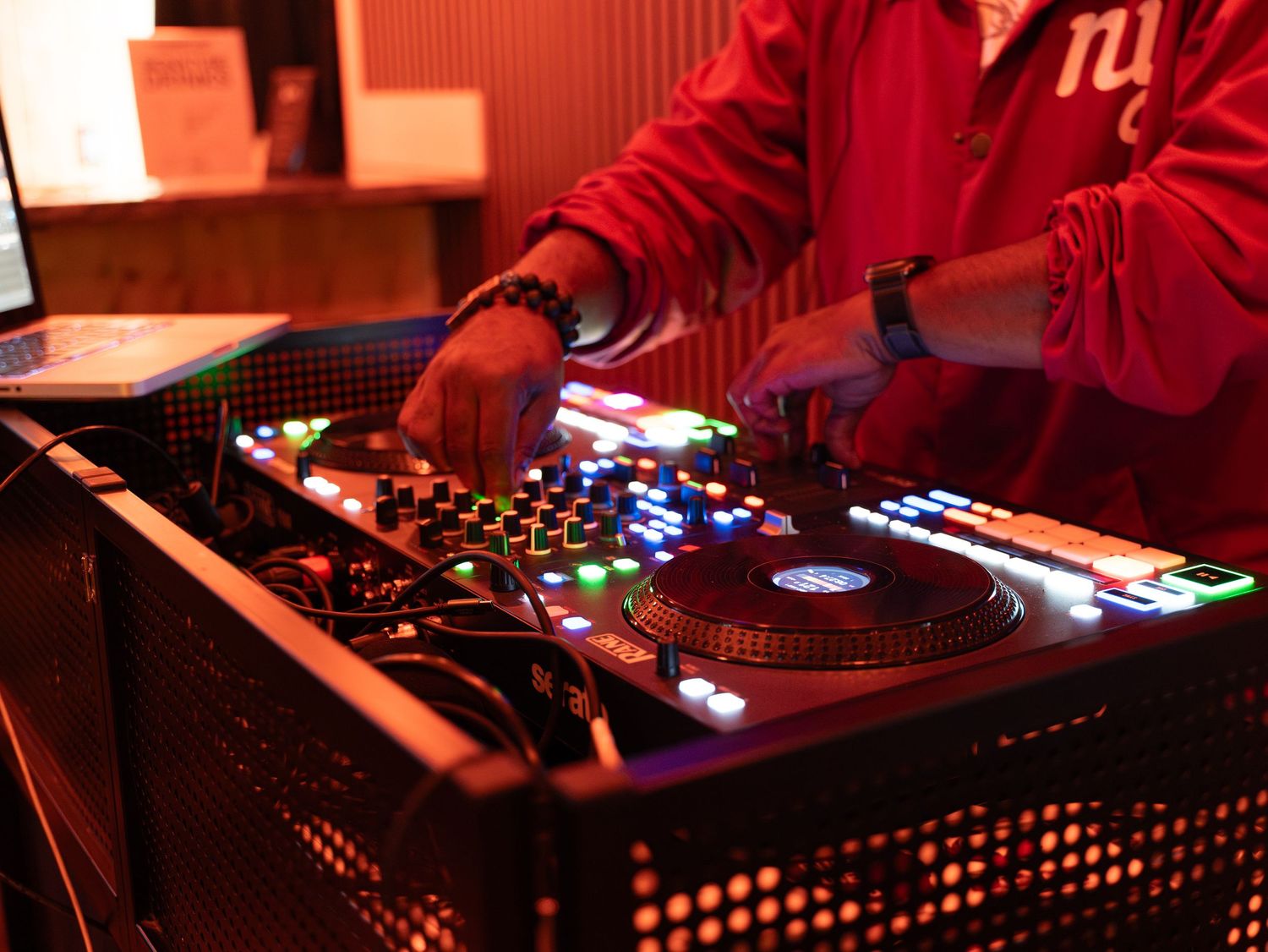 A DJ mixing deck setup with colorful LED lights and control knobs in a dark nightclub environment.