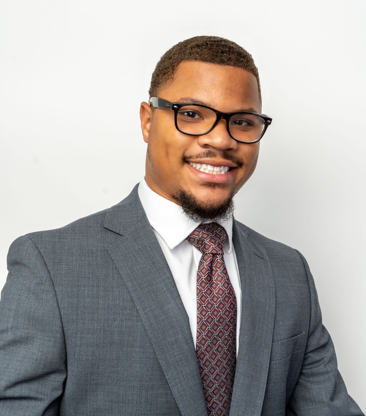 Professional headshot of person in grey suit and glasses against white background.