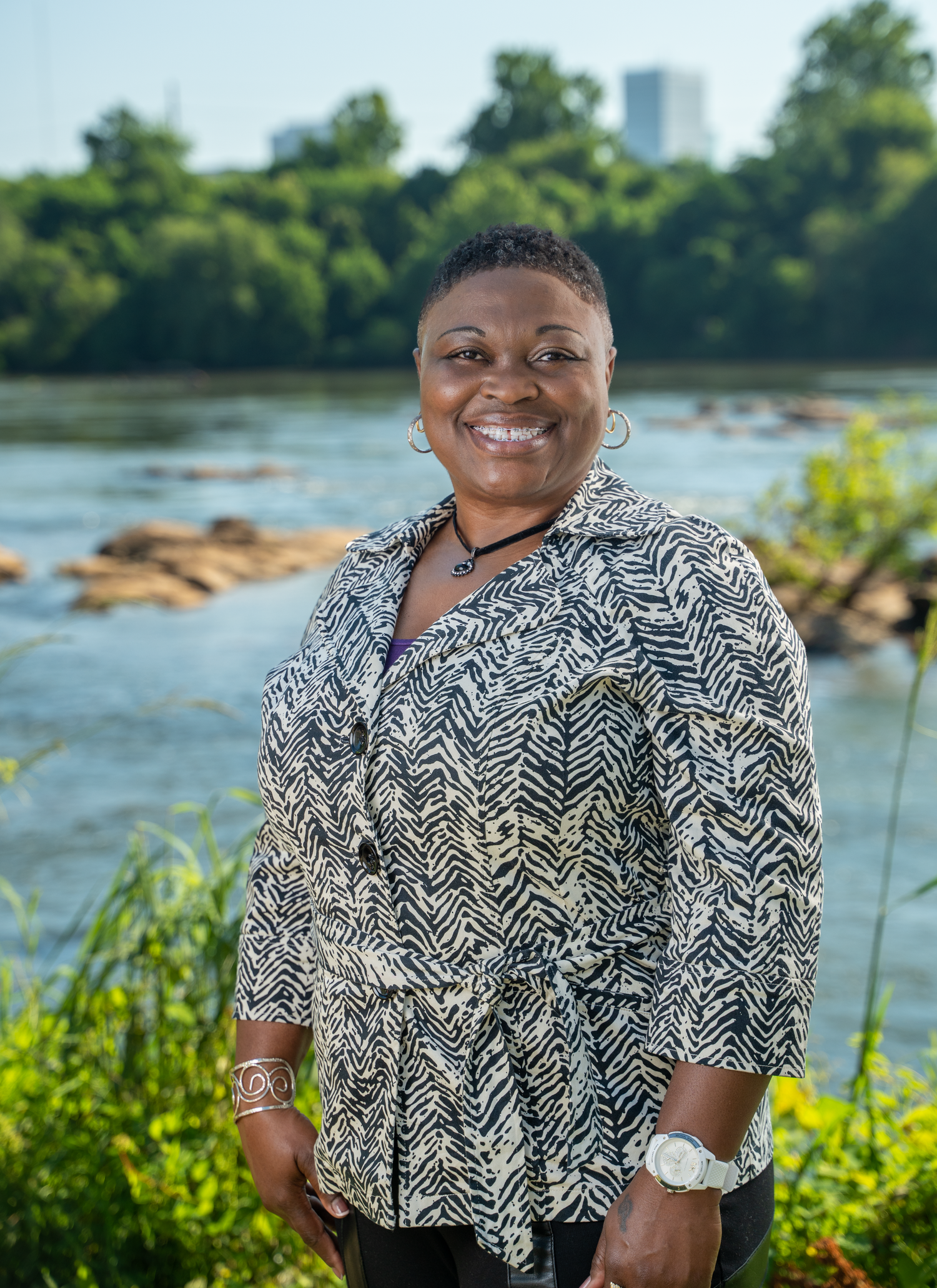 Casual outdoor portrait session near a lake with urban skyline visible in background.