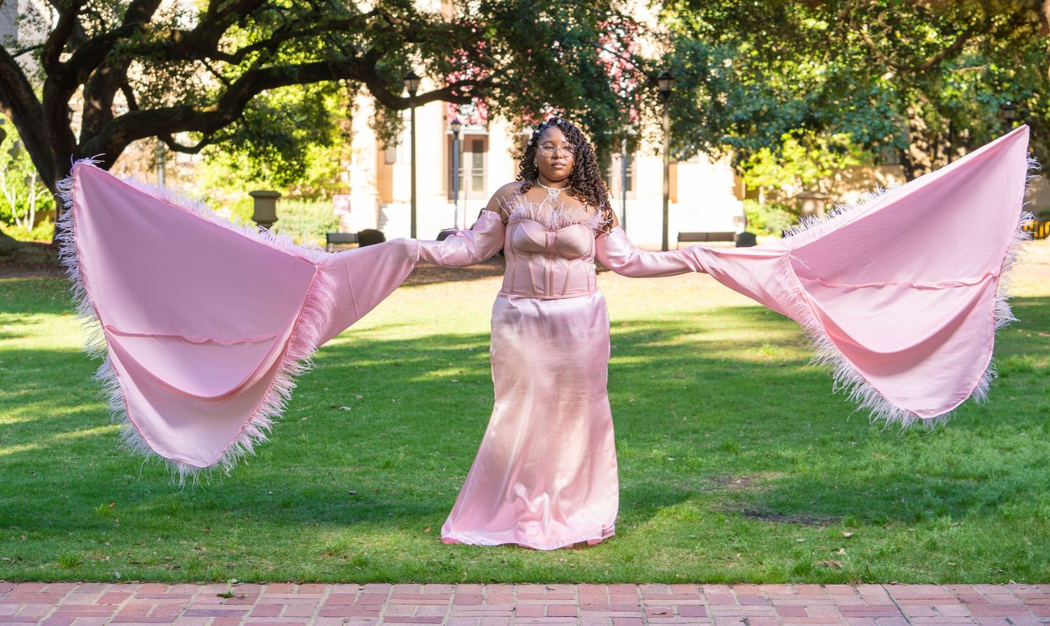 Person in flowing pink dress twirls with fabric panels in sunlit garden setting.