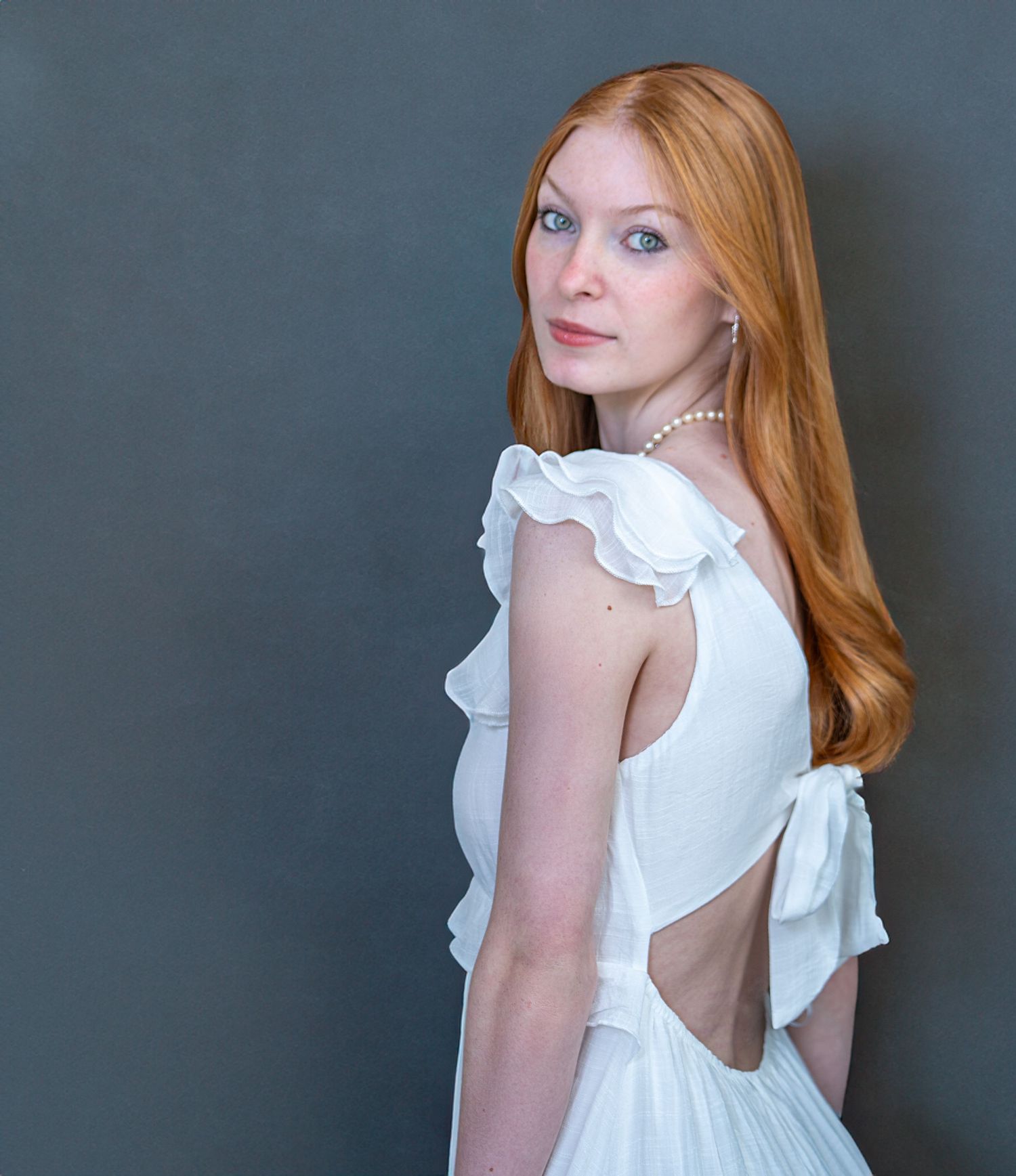 White ruffled dress photographed against a dark grey background in soft lighting.