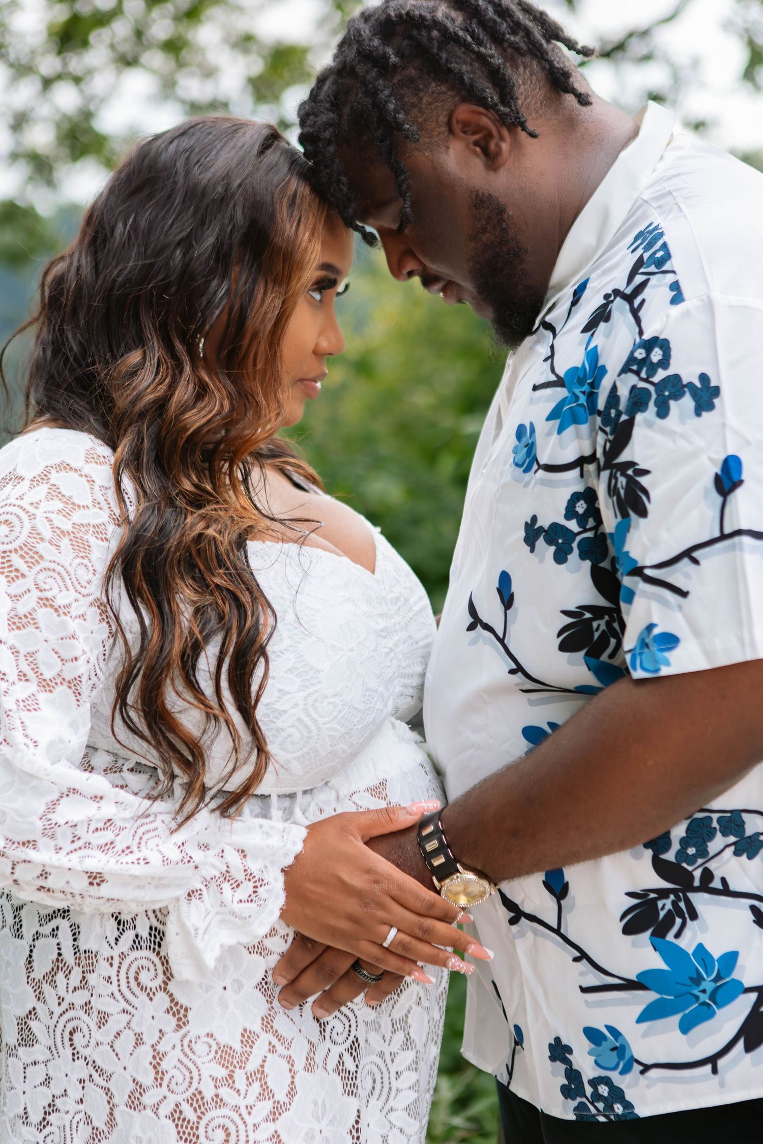 A romantic couple embracing in white and blue floral outfits for their maternity photoshoot outdoors in Youngstown, Ohio.