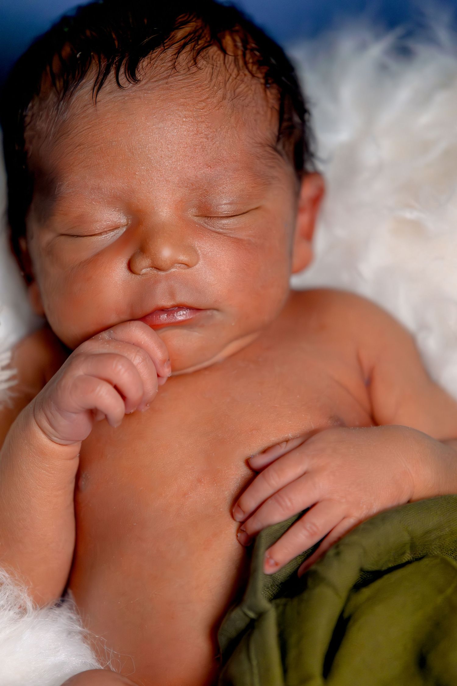 A sleeping newborn baby wearing an olive green swaddle blanket rests peacefully against white bedding in Youngstown, Ohio.