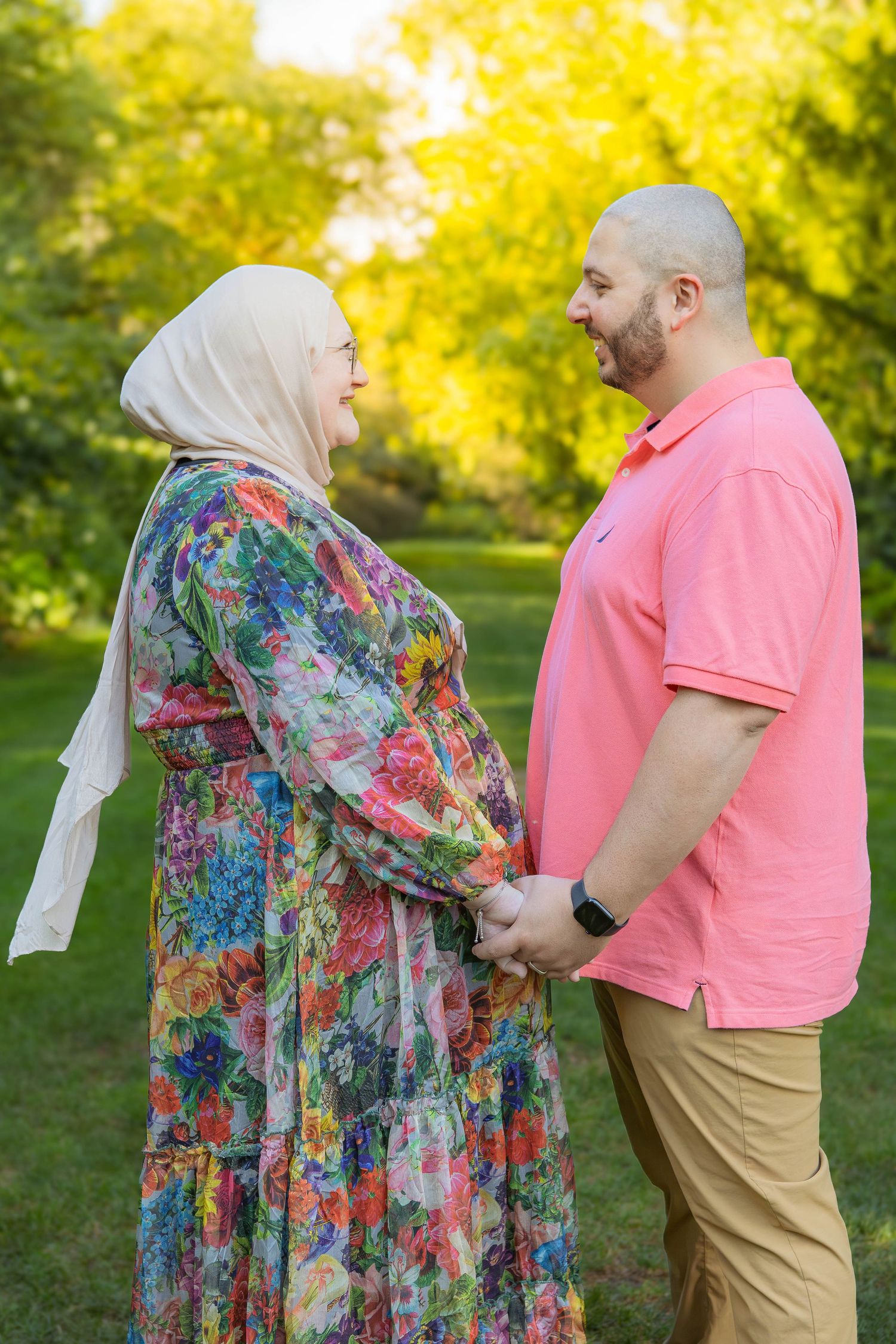 A couple stands together in a sunny park, with one wearing a floral dress and the other in a pink polo shirt and khakis in Youngstown, Ohio.